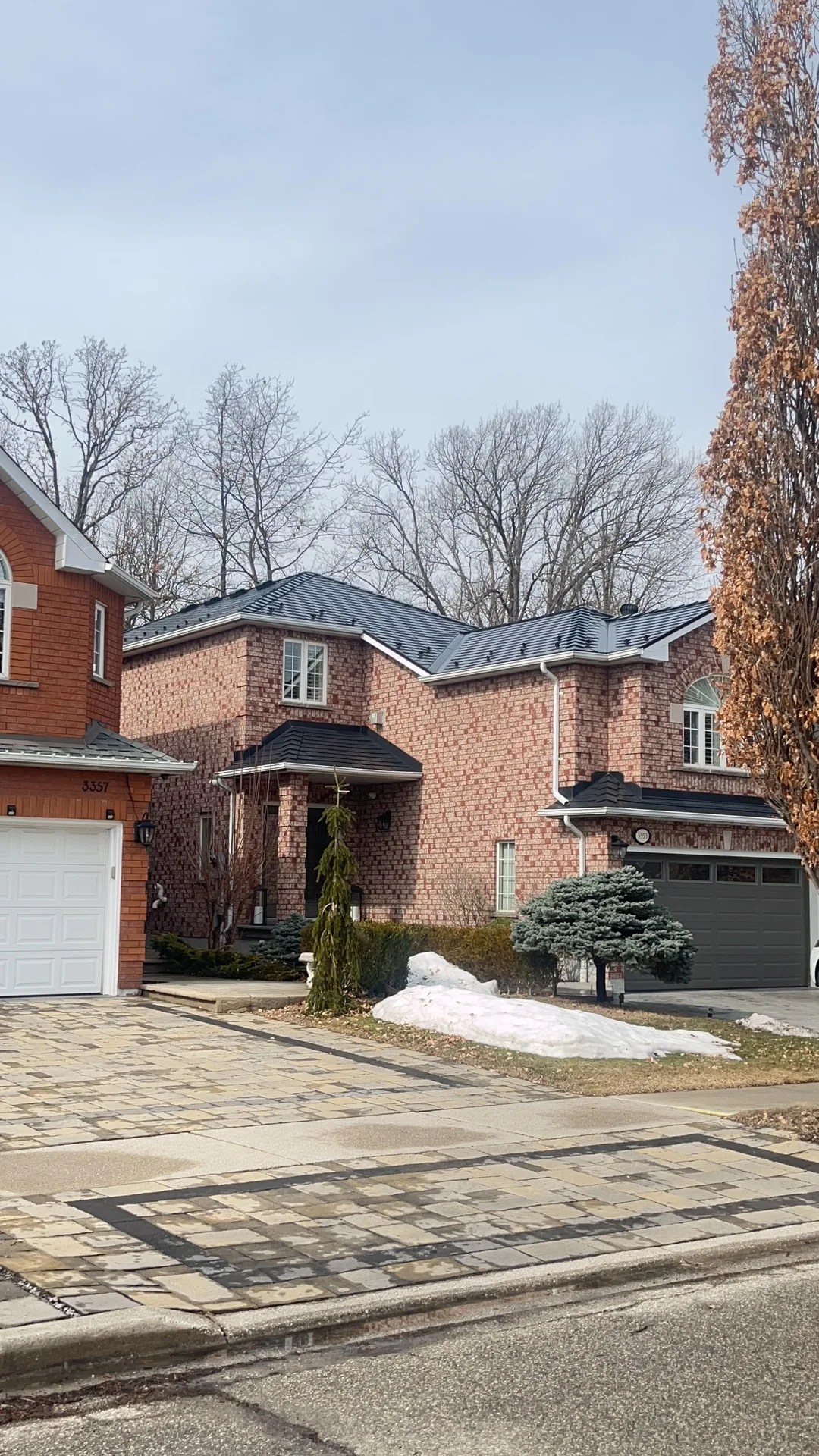 Black Interlock Slate aluminum roof on a red brick two-storey home with dormers among tall trees, Mississauga, Ontario