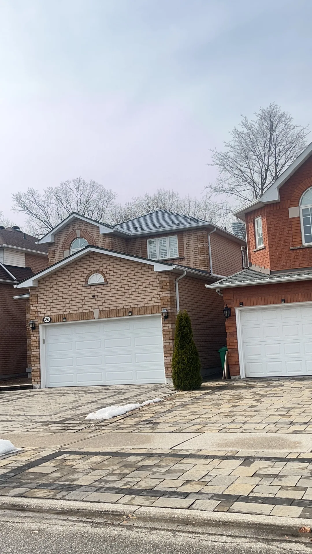Black Interlock Slate aluminum roof on a two-storey red brick home with white trim among suburban, Mississauga, Ontario