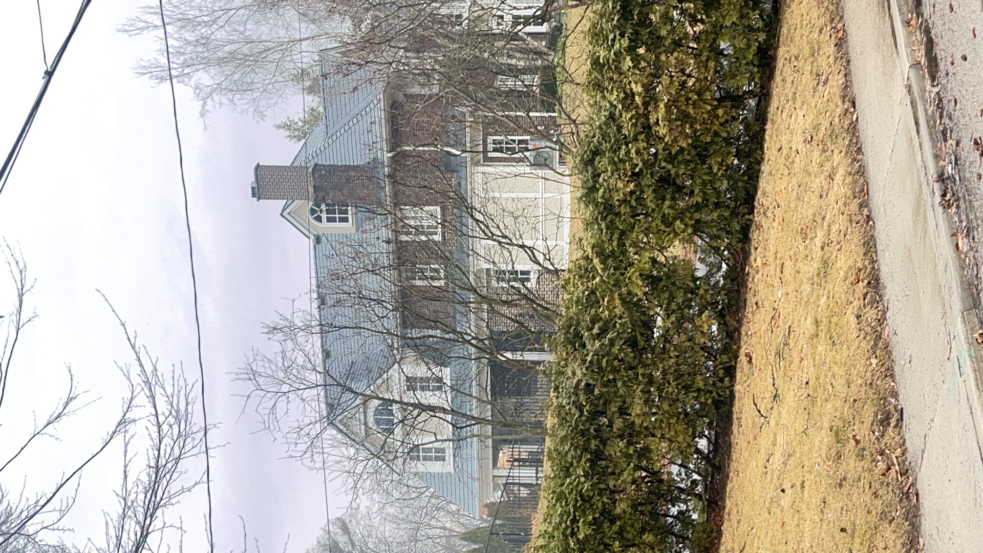 Two-storey colonial brick home in Burlington ON with steep deep charcoal Interlock aluminum slate roof, twin dormers, and brick chimney, viewed from street.