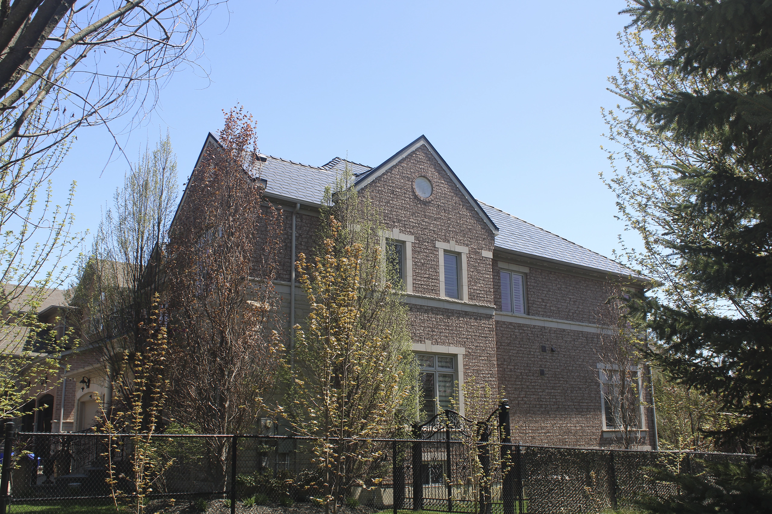 Two-storey Tudor-style brick home in Woodbridge ON with Interlock black aluminum slate metal roofing featuring steep gabled dormers and multi-plane roof.
