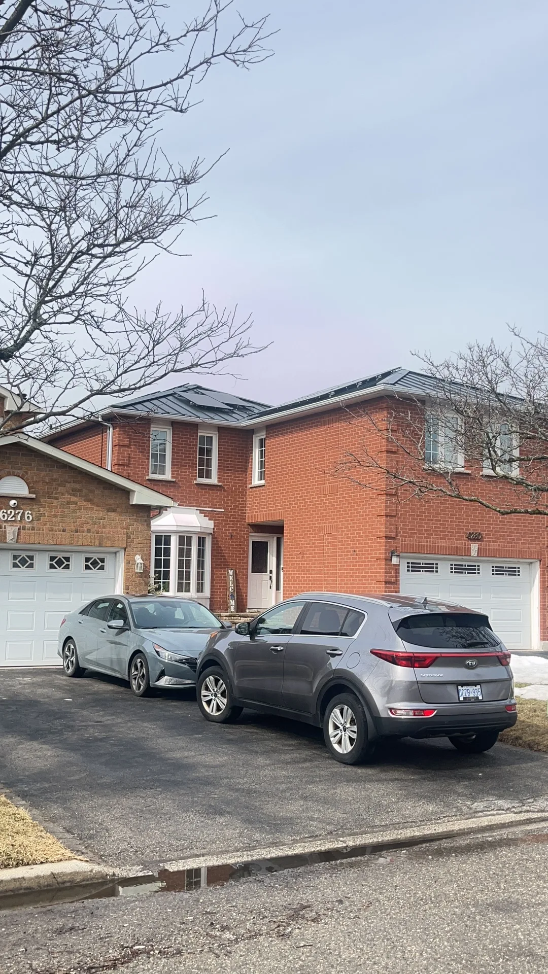 Black Interlock Standing Seam aluminum roof on a two-storey brick home with a metal roof among tall trees, Mississauga, Ontario