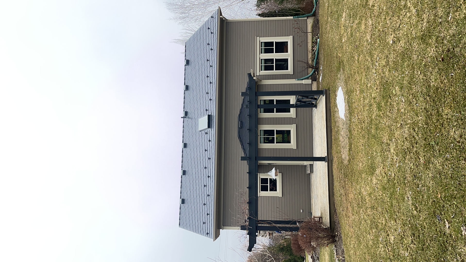 Rear elevation of a Craftsman-style home in Ravenna, ON featuring Interlock black aluminum slate metal roofing with snow guards, skylights, and a dark pergola over a rear patio.