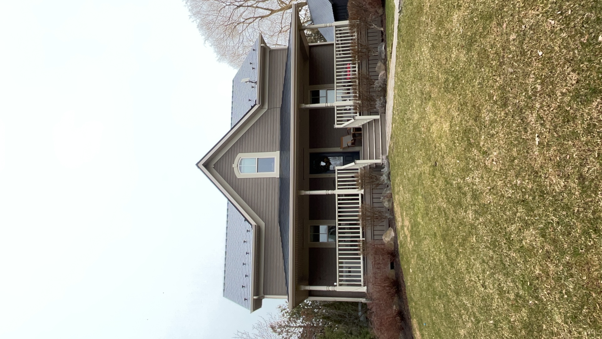 Two-storey farmhouse in Ravenna, ON with black Interlock aluminum slate metal roof, front dormer, wrap-around porch, and snow guards visible on steep gable.