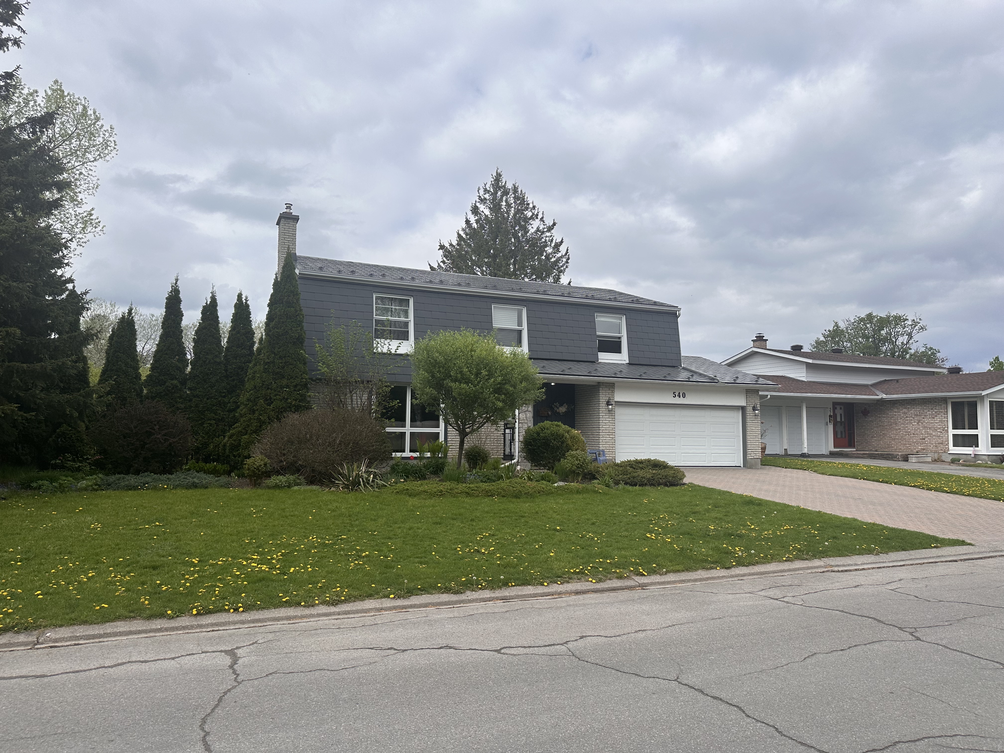 Two-storey colonial-style home in Ottawa with Interlock charcoal grey aluminum shingle roof, chimney, brick lower facade, and double garage.