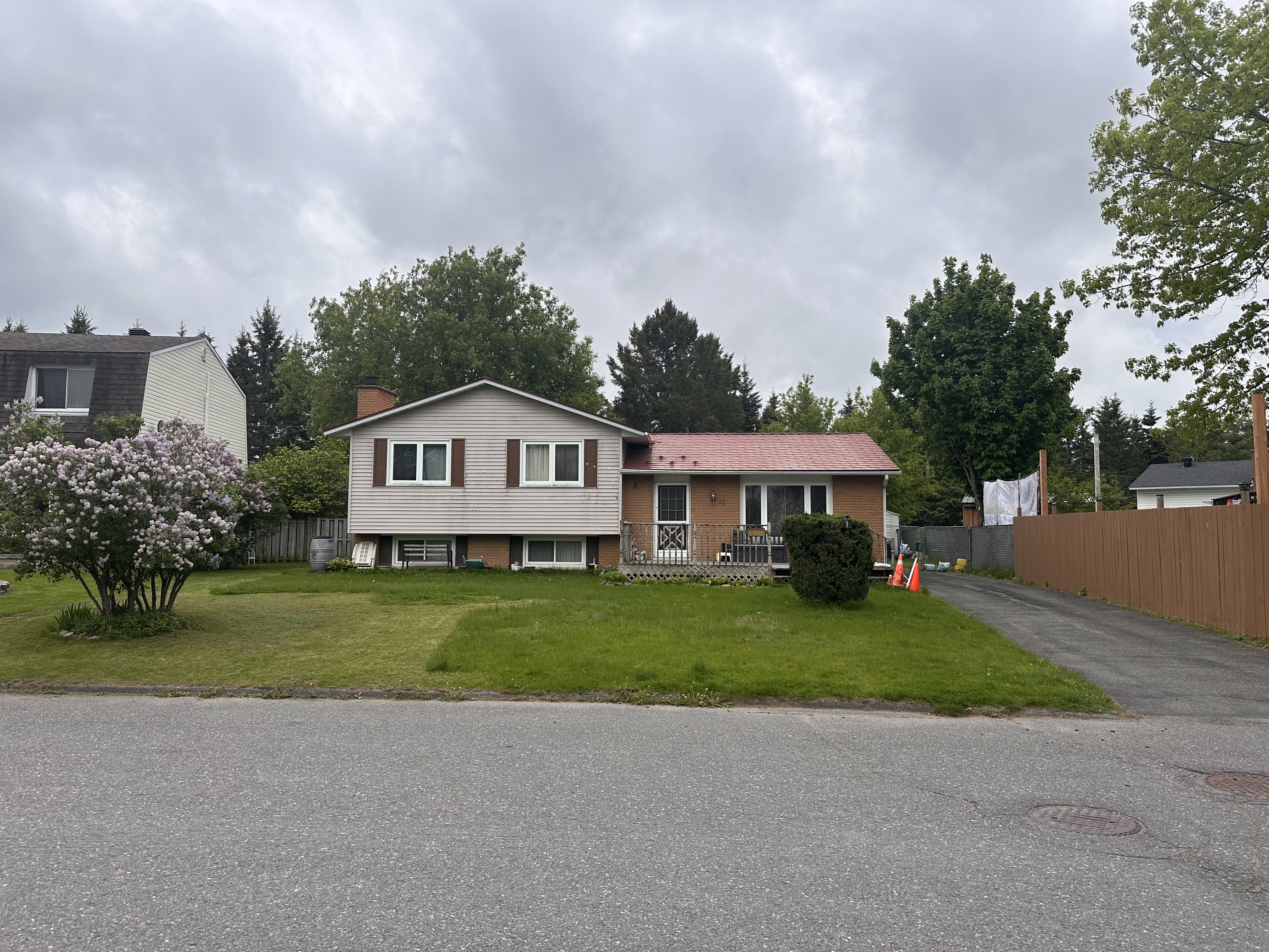 Street view of a split-level ranch home in Munster, ON featuring a tile-red Interlock aluminum shingle roof with brick chimney, surrounded by mature trees.