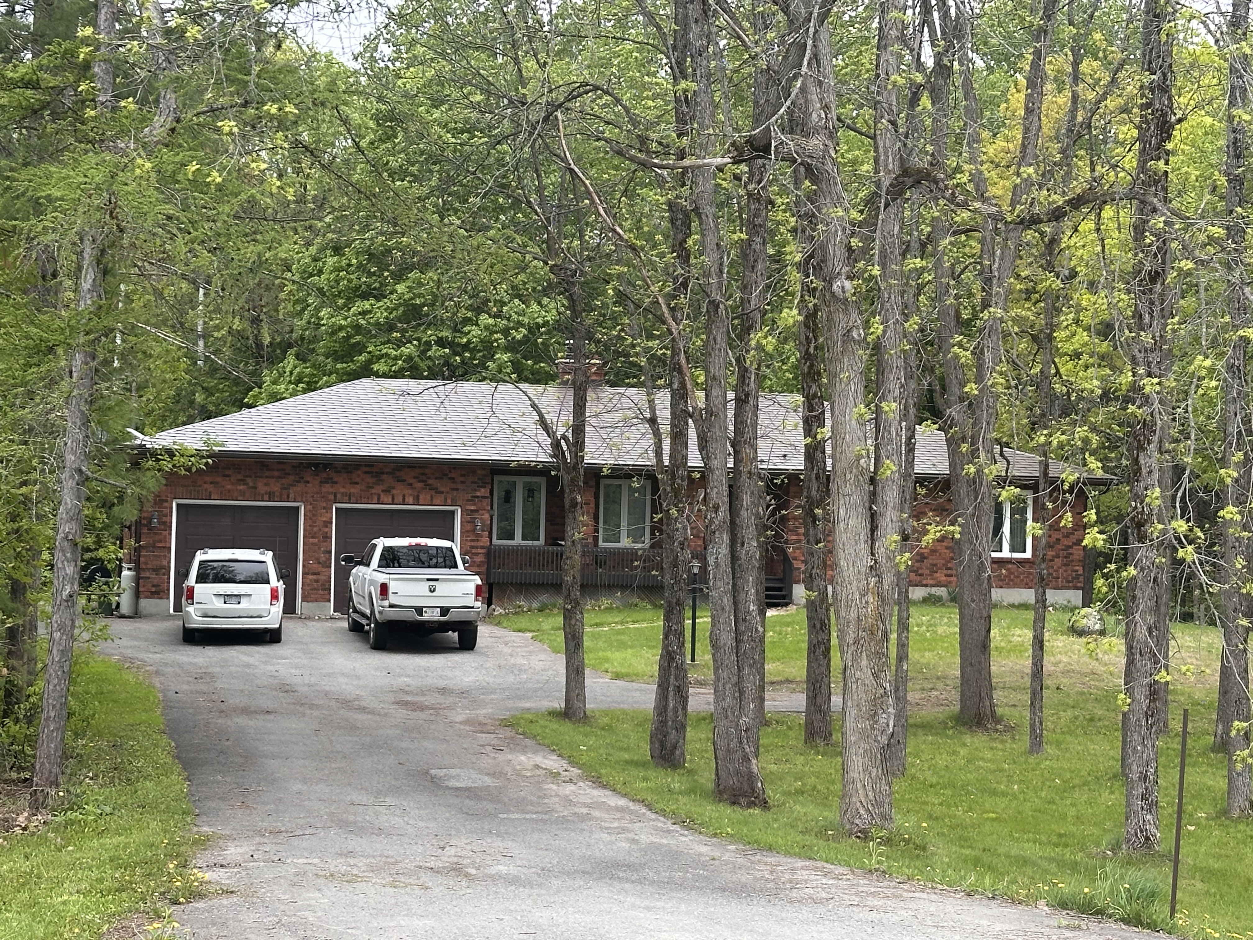 Single-storey brick ranch home in Richmond ON with Colonial Brown Interlock aluminum shingle roof, hip profile, viewed through mature trees from front-left.