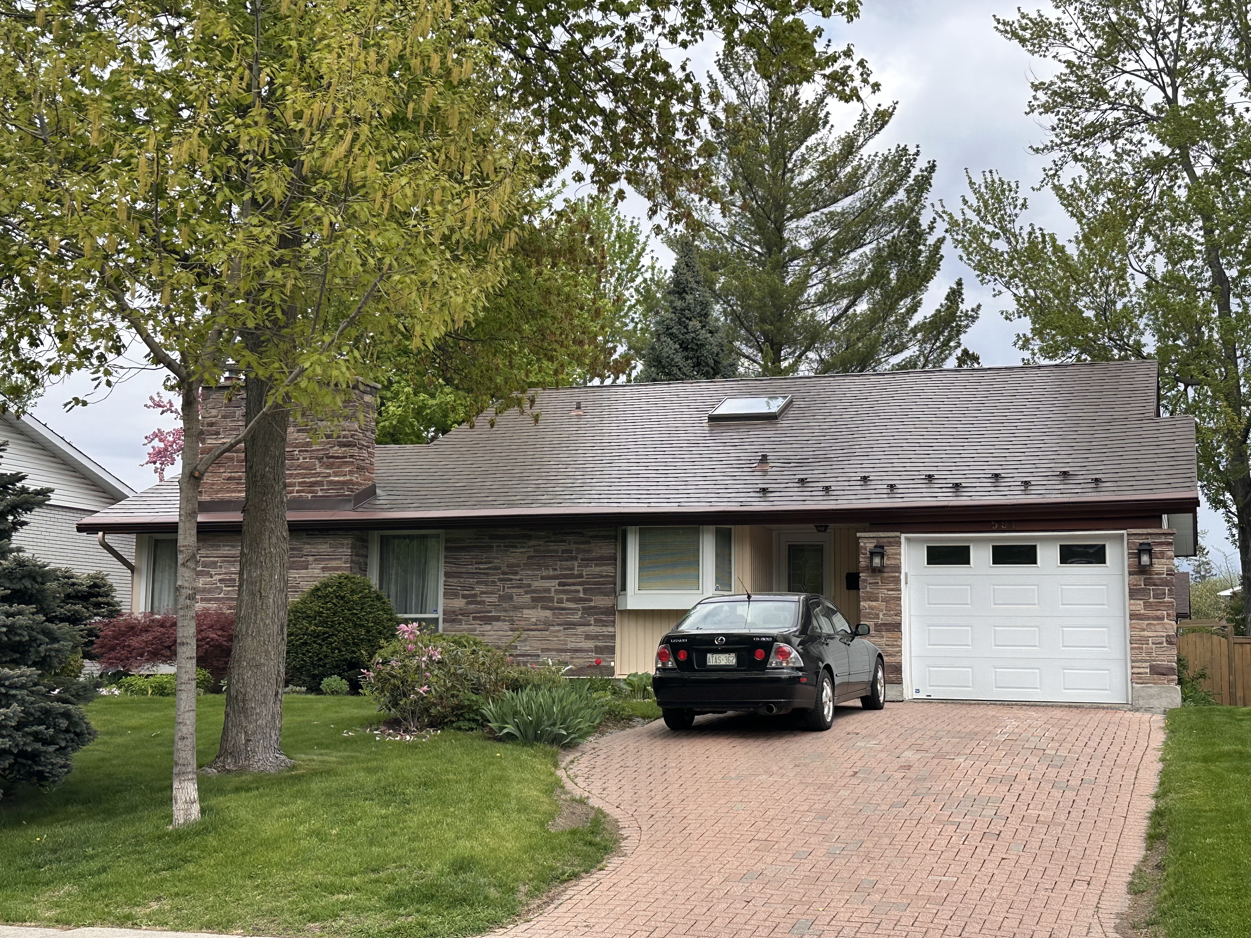 Single-storey ranch home in Ottawa with a low-pitch Colonial Brown Interlock aluminum shingle roof, stone facade, skylight, and chimney.