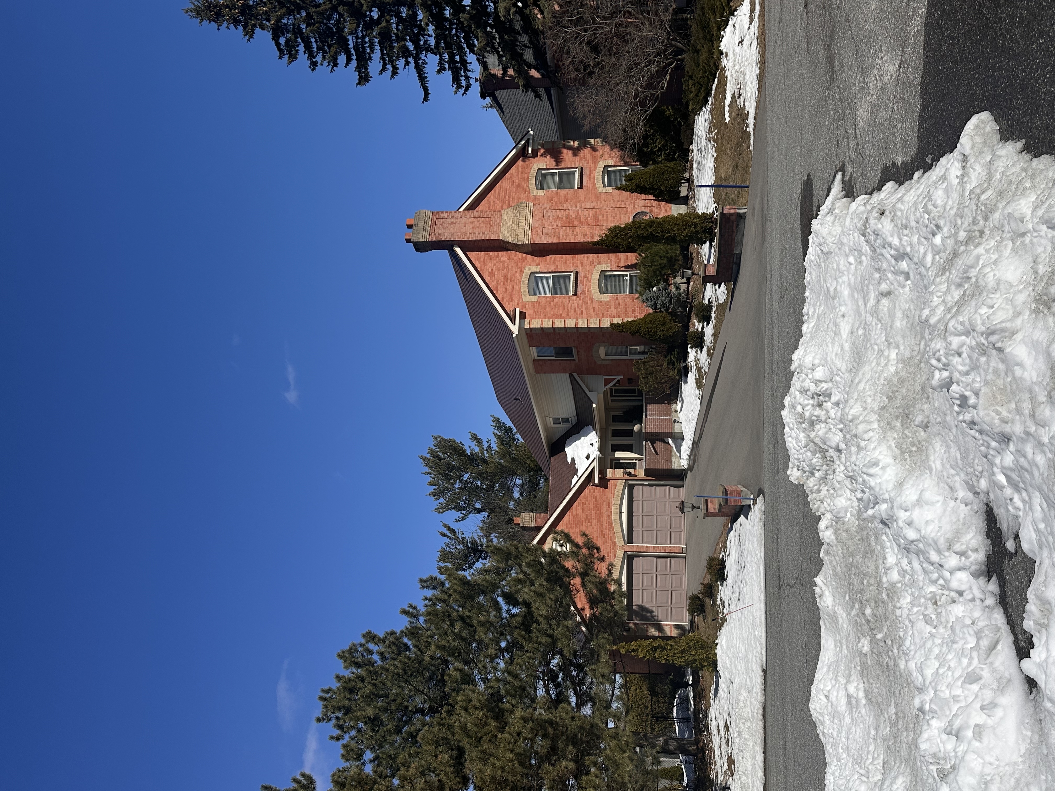 Two-storey red brick colonial home in Stittsville ON with Interlock Tile Red aluminum slate metal roof and prominent chimney, photographed in winter.