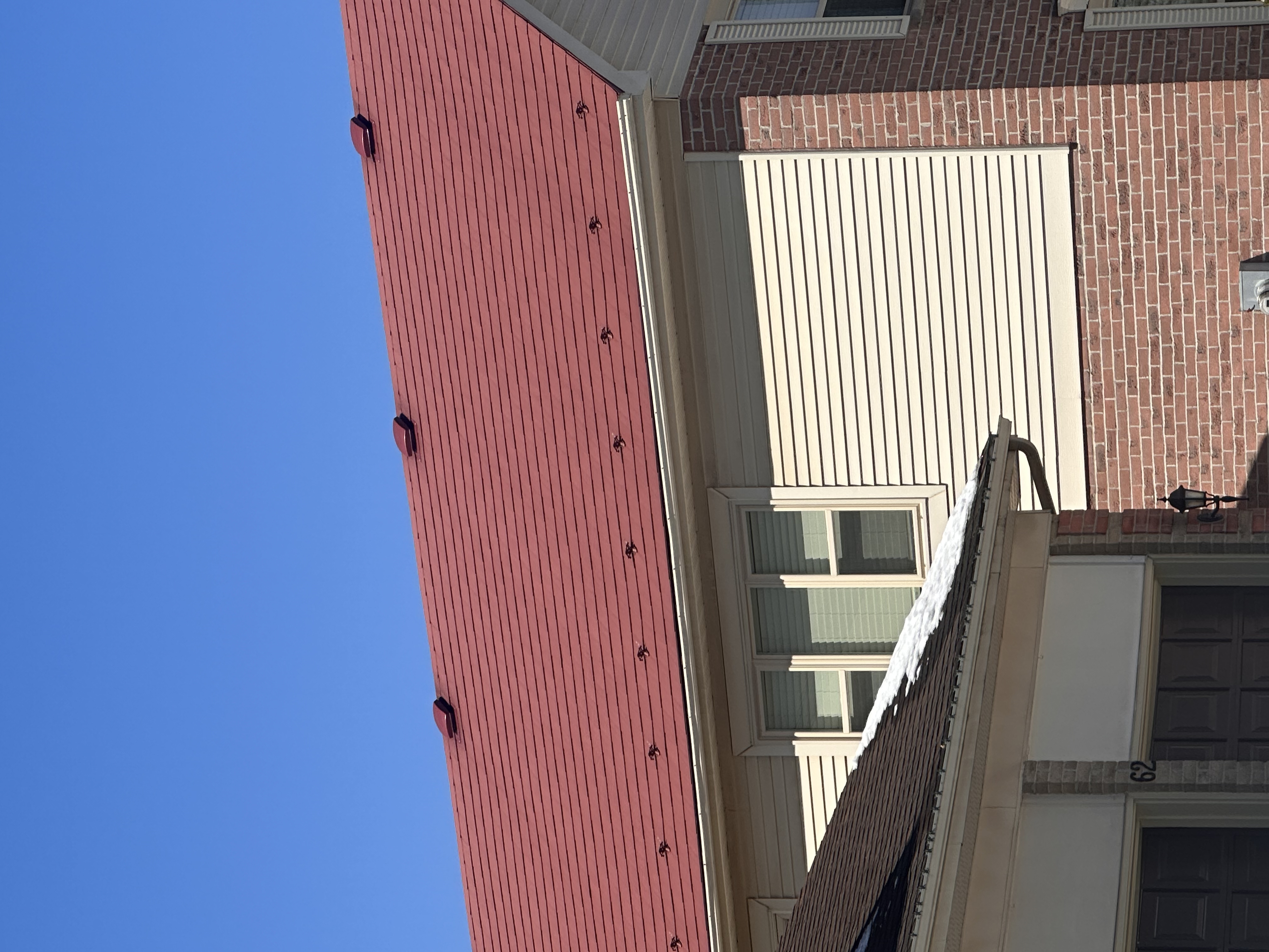 Tile red Interlock aluminum shingle metal roof on a 2-storey brick and vinyl colonial home in Stittsville, ON, under a clear blue sky.