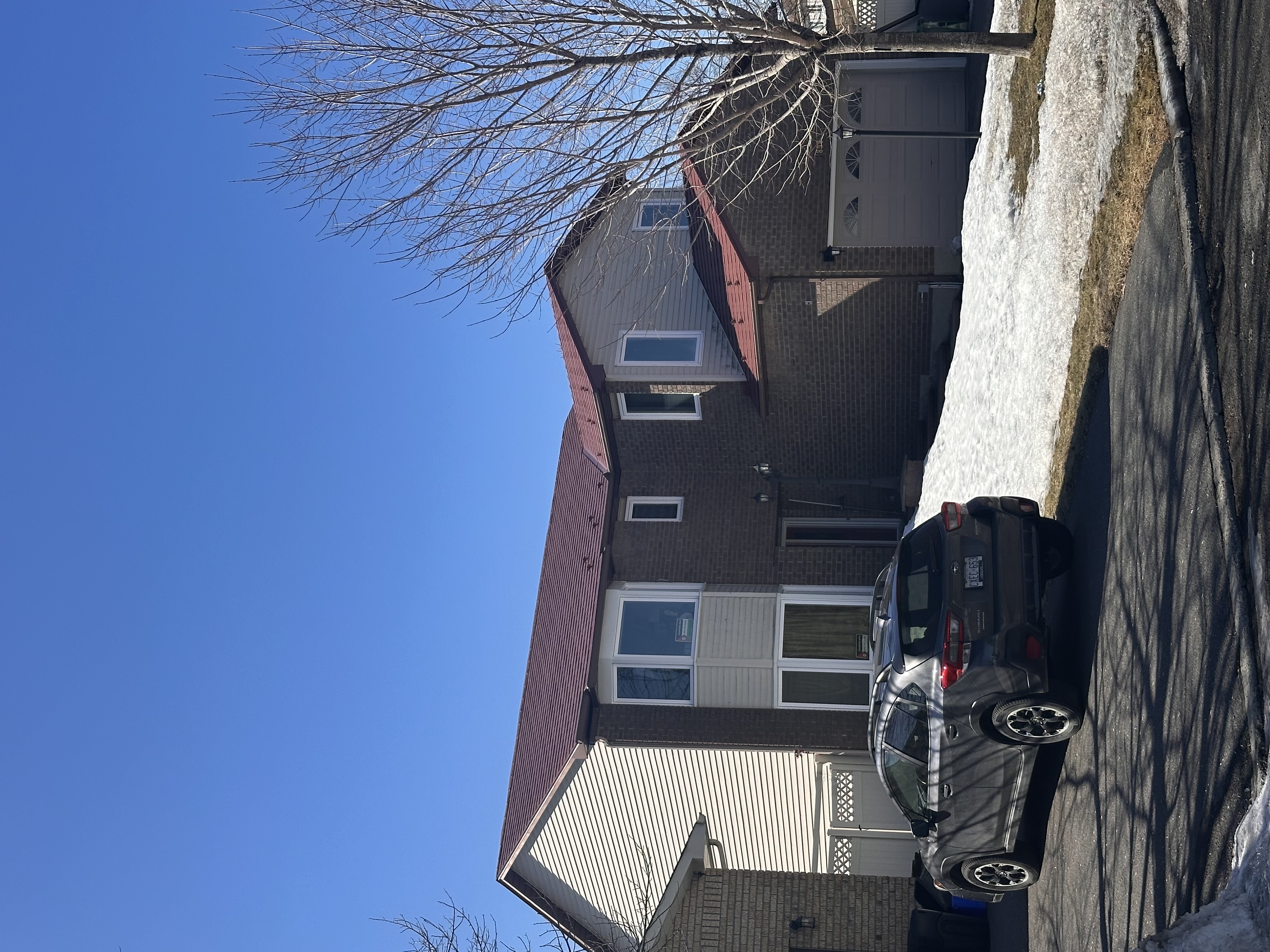 Two-storey brick suburban home in Orleans ON with Interlock Tile Red aluminum shingle metal roofing on a multi-hip complex roof, clear winter sky.