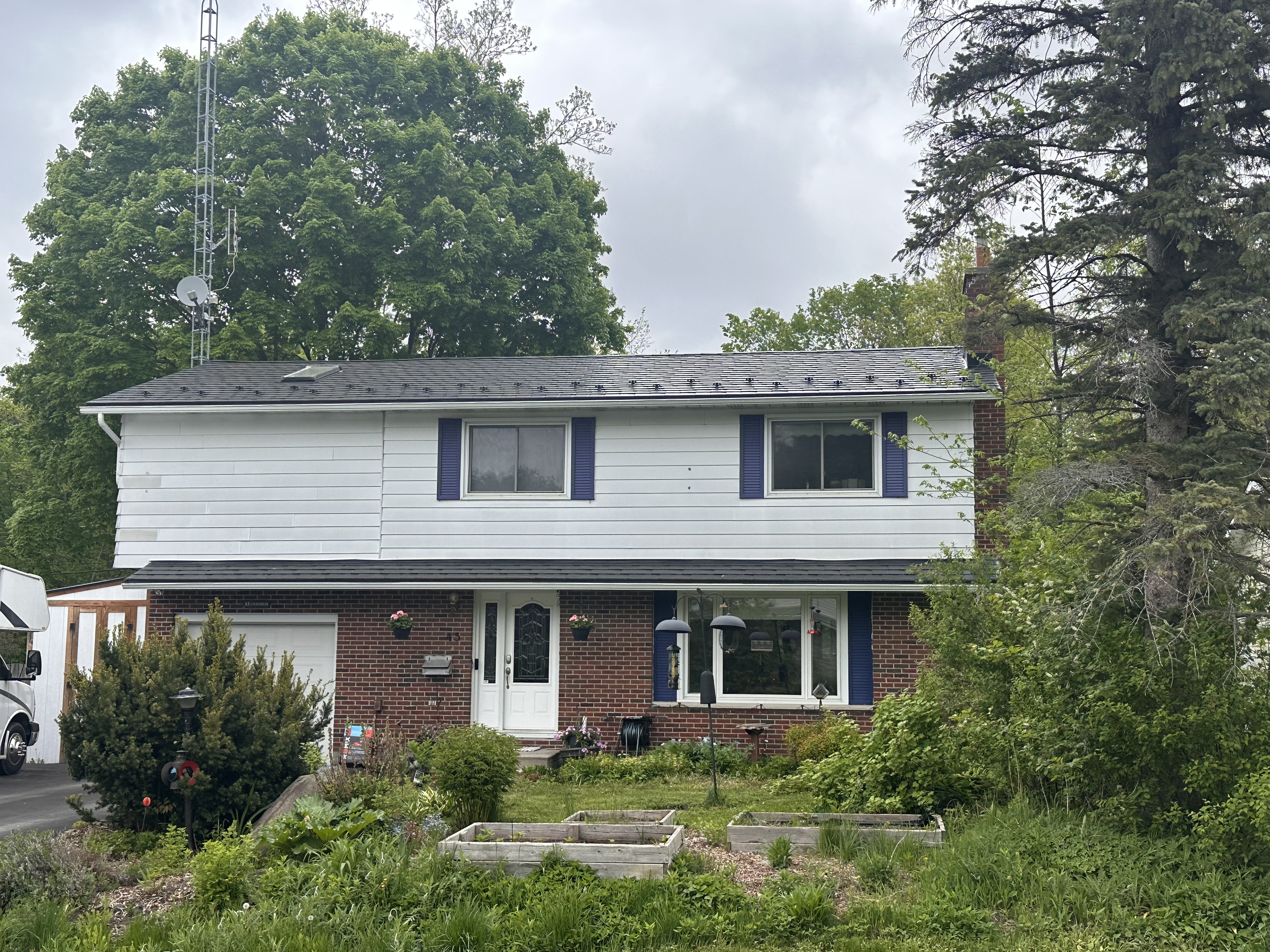 Two-storey colonial home in Munster ON with black Interlock aluminum slate metal roofing, white vinyl upper siding, and red brick lower façade.