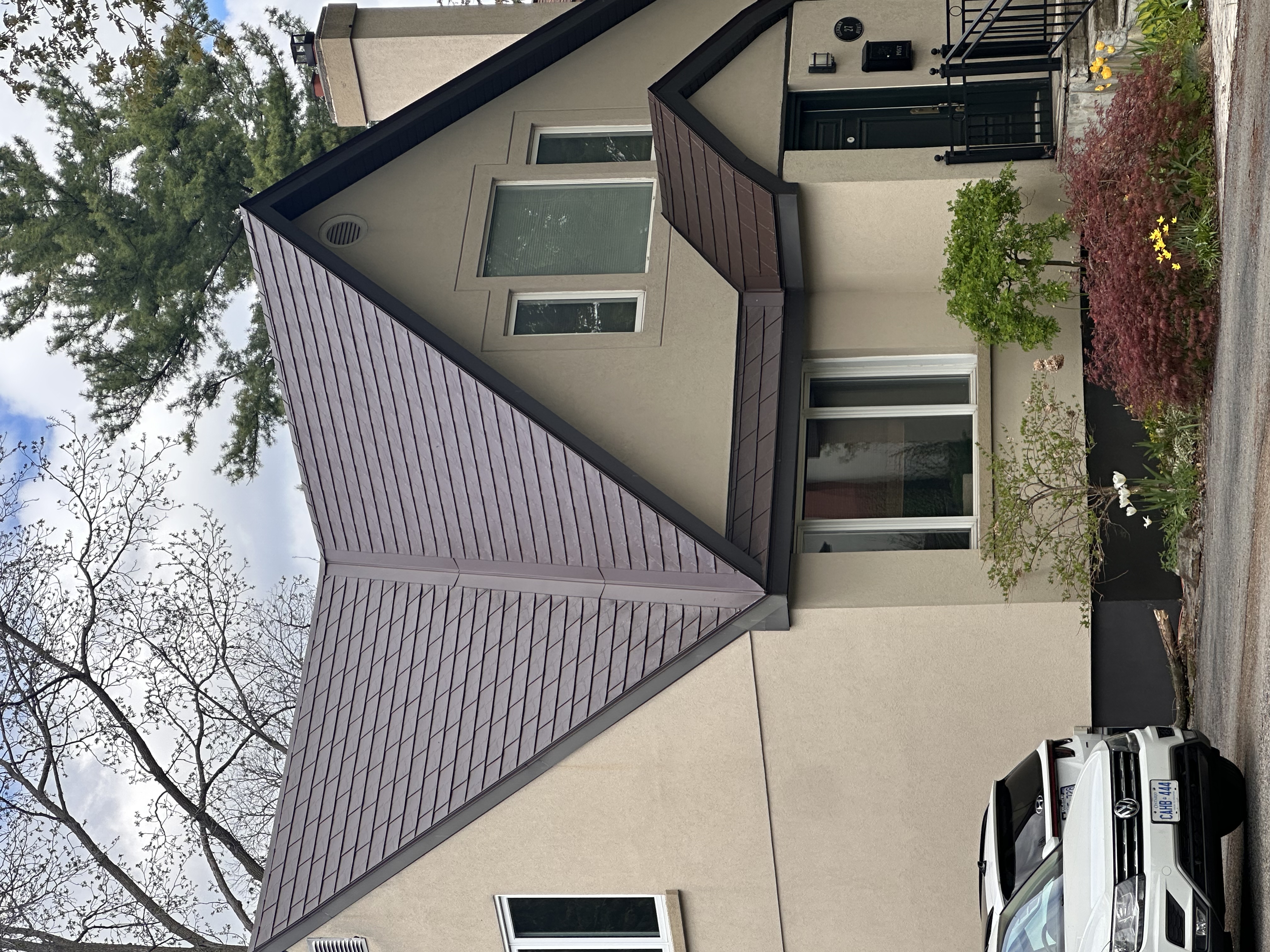 Two-storey Tudor-style home with a complex steep-pitched Colonial Brown Interlock aluminum slate roof featuring dormers, valleys, and a chimney.