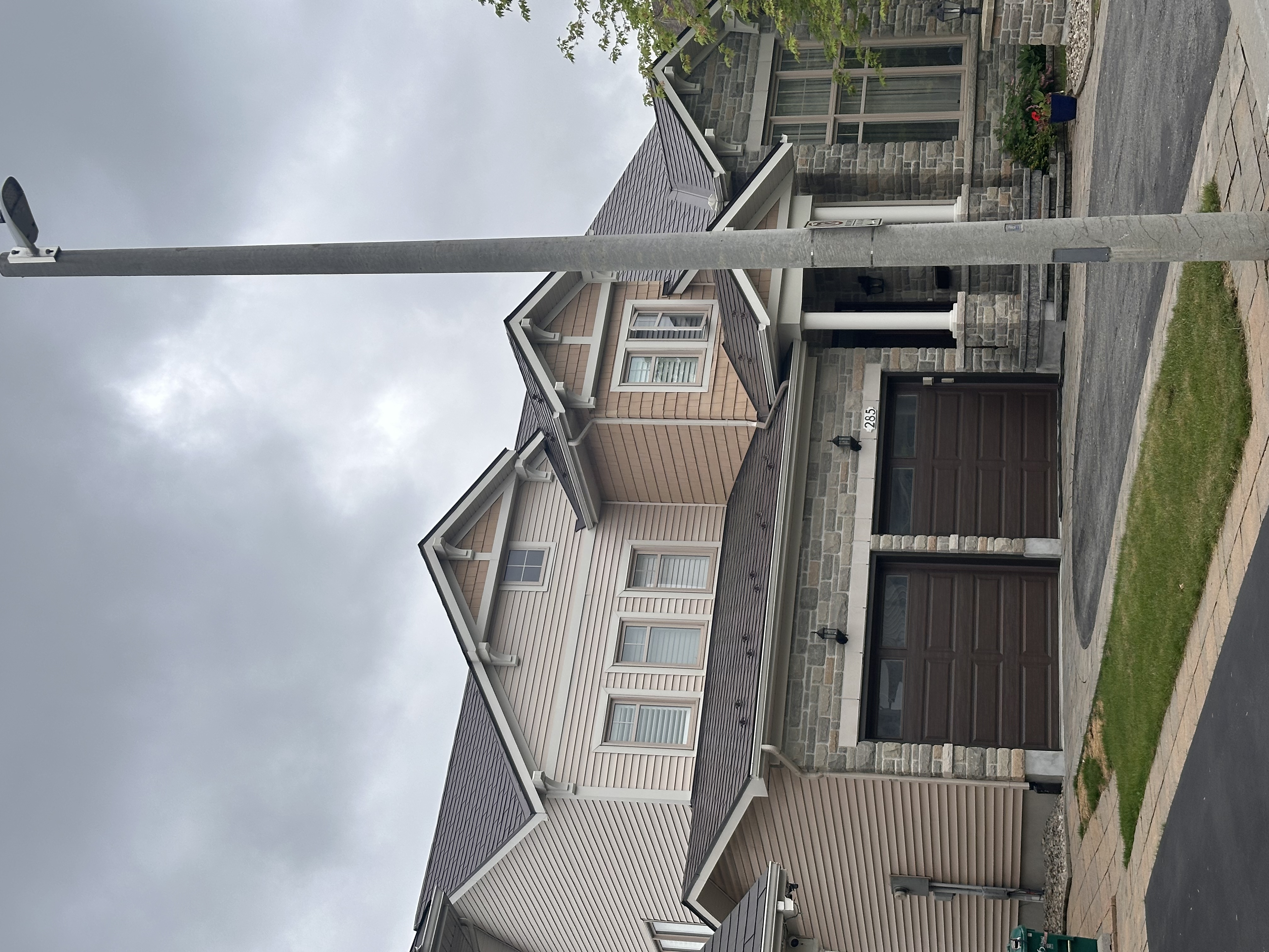 Two-storey Craftsman home at 285 with Interlock Tudor Brown aluminum slate roofing, multi-plane gabled roof, stone facade, and double garage.