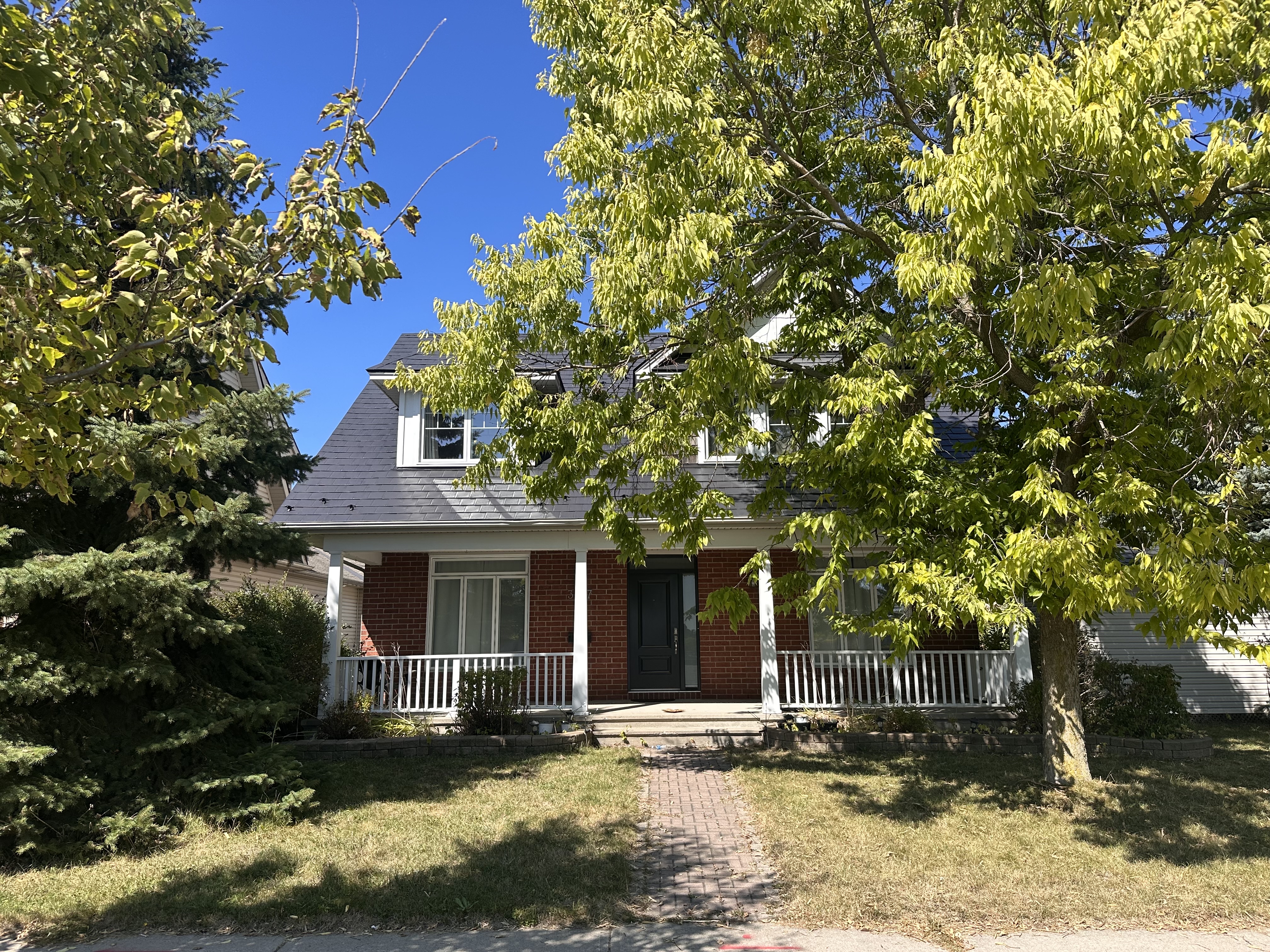 Two-storey Victorian home in Ottawa with black Interlock aluminum slate metal roofing featuring a turret and dormers, red brick facade, and covered front porch.