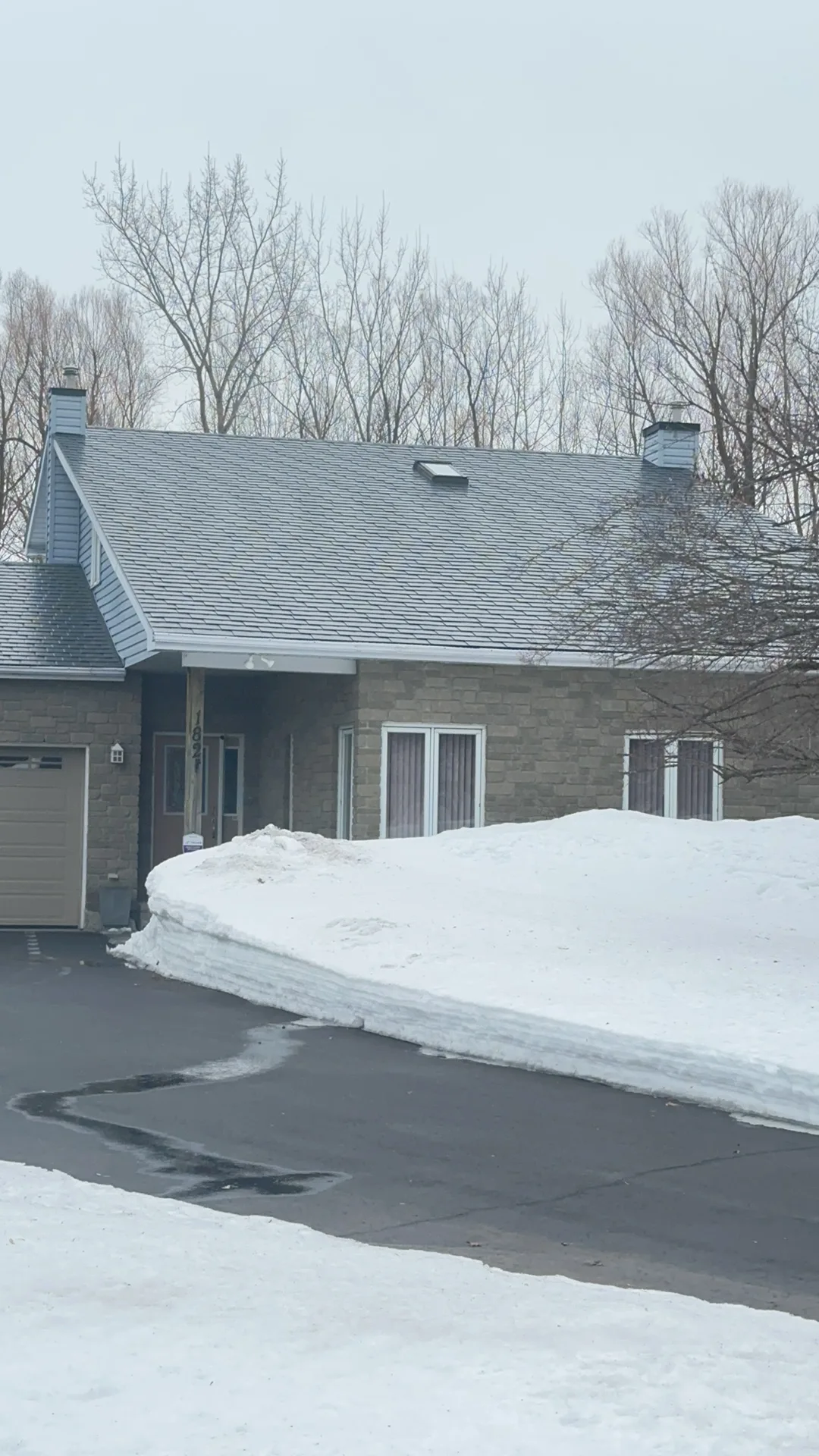 Black Interlock Slate aluminum roof on a grey brick home with a grey metal roof in the woods, Navan, Ontario