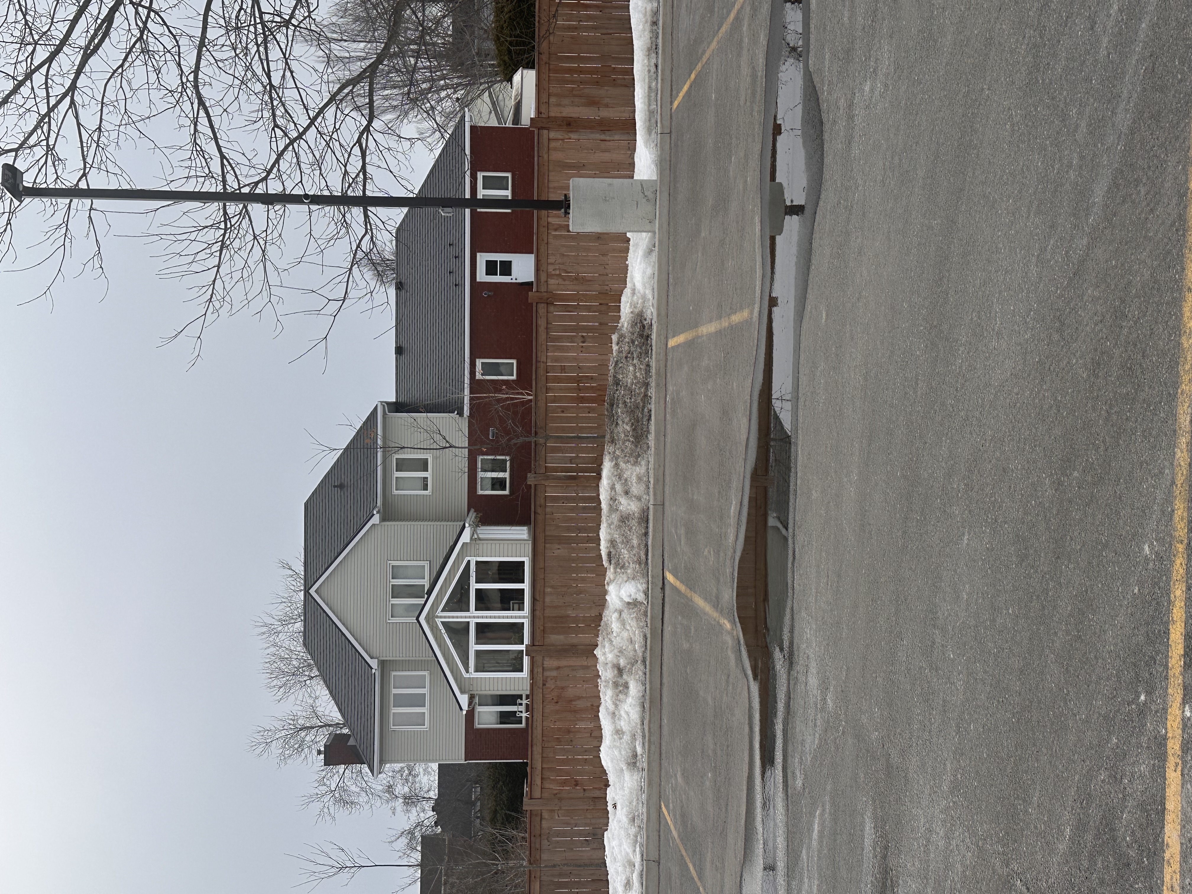 Rear elevation of a two-storey suburban home in Navan, ON with dark slate-profile Interlock aluminum roofing, red brick lower level, and gabled sunroom addition.