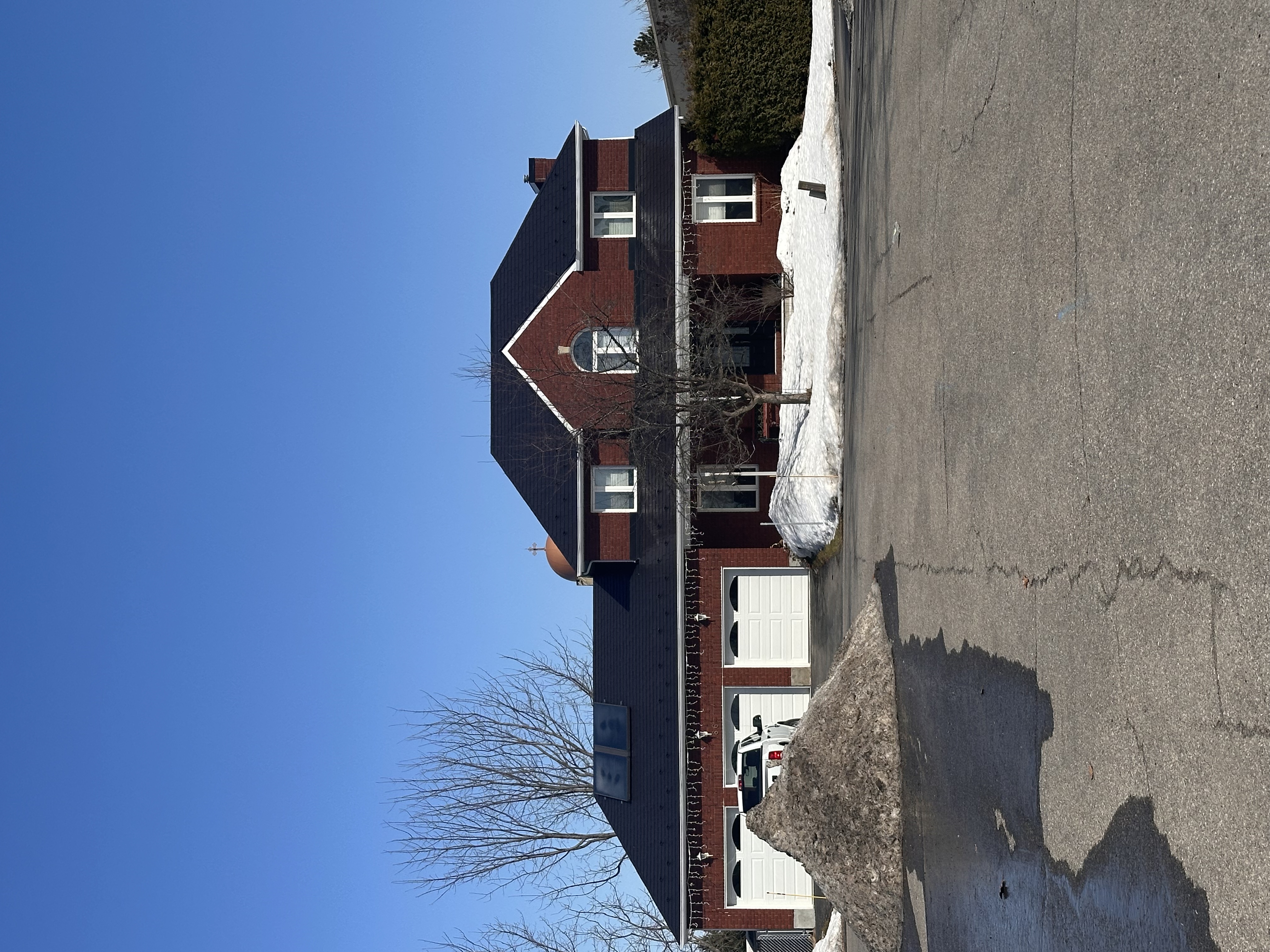 Two-storey red brick Colonial home in Navan ON with black Interlock aluminum slate roofing, turret, skylights, and triple-car garage in winter.