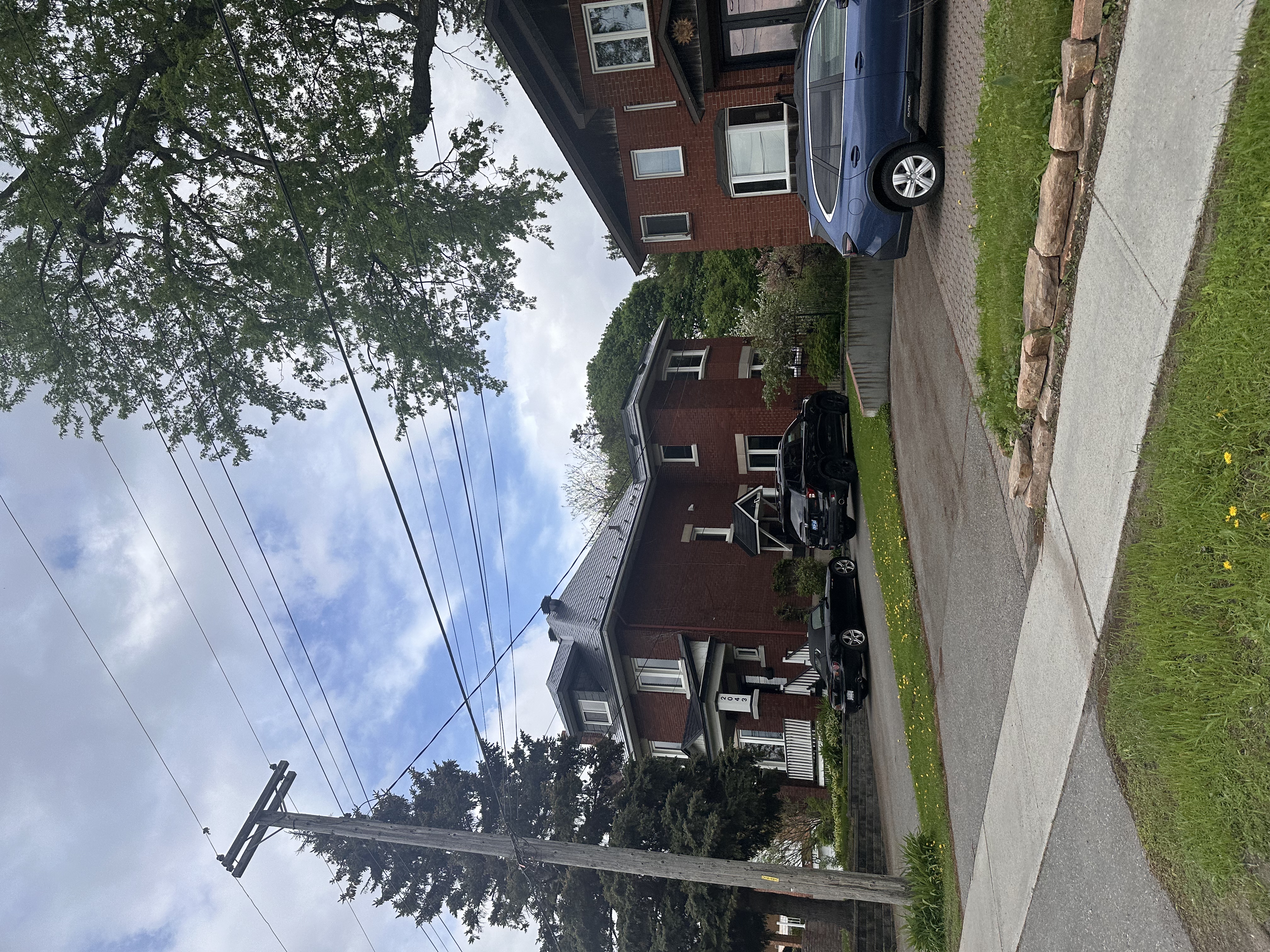 Street-view of a red-brick heritage home in Ottawa with a steep black Interlock aluminum slate metal roof, multi-hip profile, surrounded by mature trees.