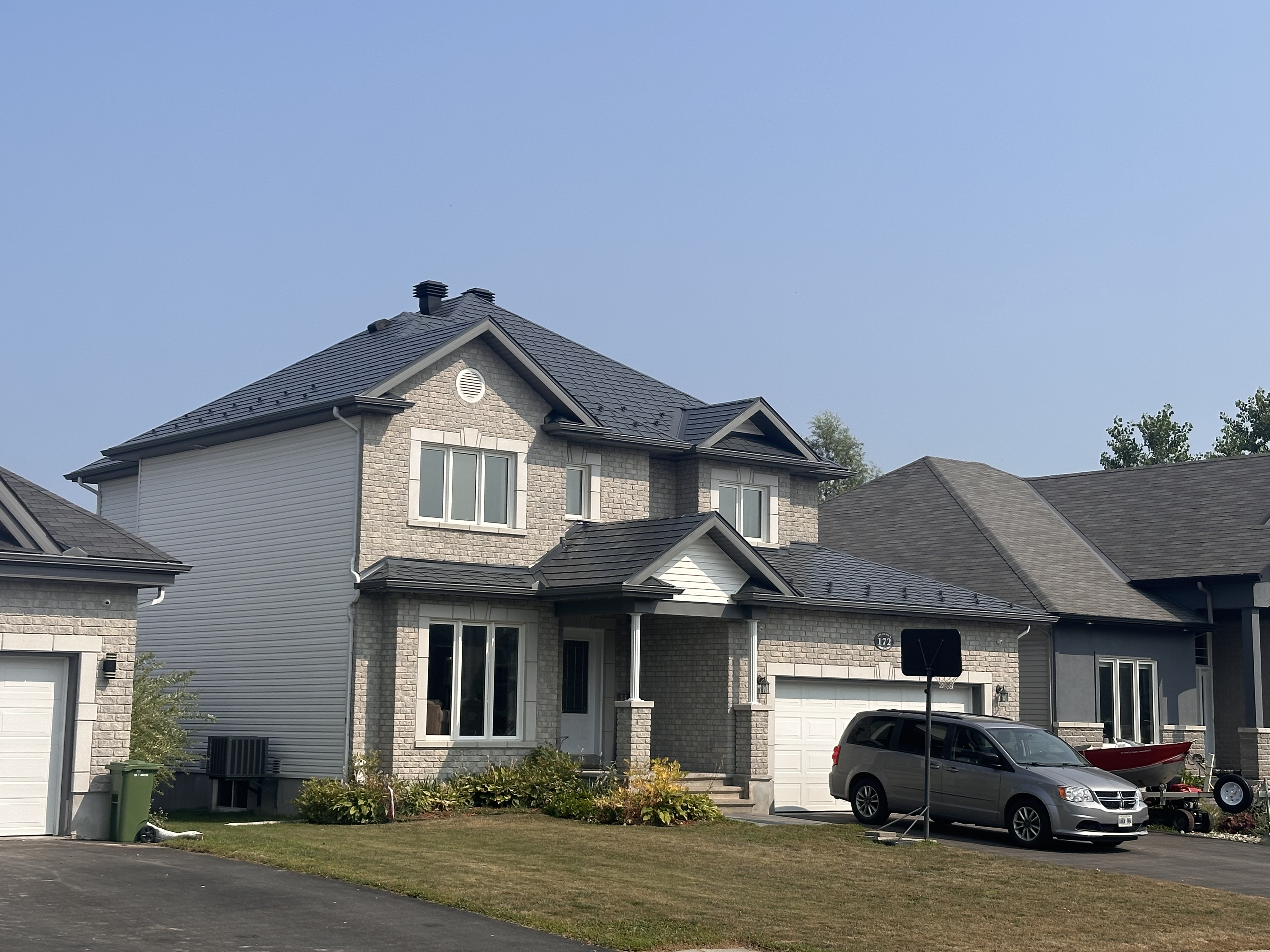Two-storey suburban home in Russell, ON with Interlock deep charcoal aluminum slate metal roofing on a complex multi-hip roof with dormers and stone facade.