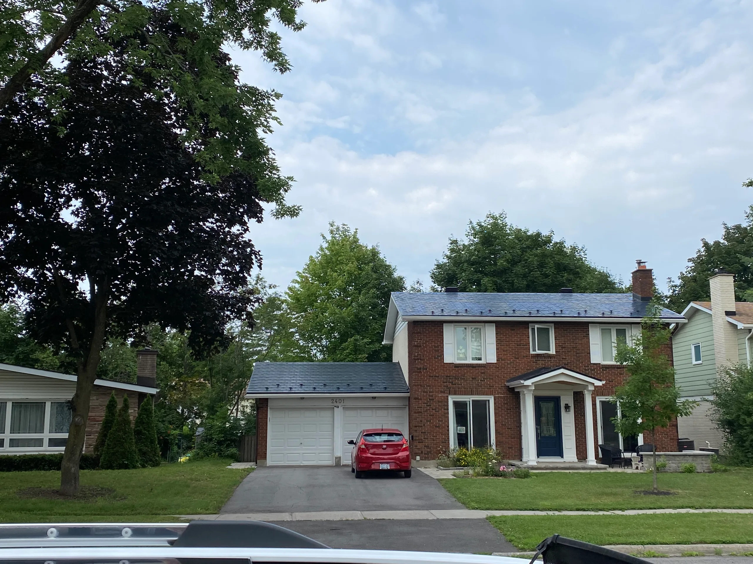 Two-storey Colonial brick home in Ottawa with Interlock black aluminum slate metal roofing on main house and attached garage, set in a leafy suburban neighbourhood.