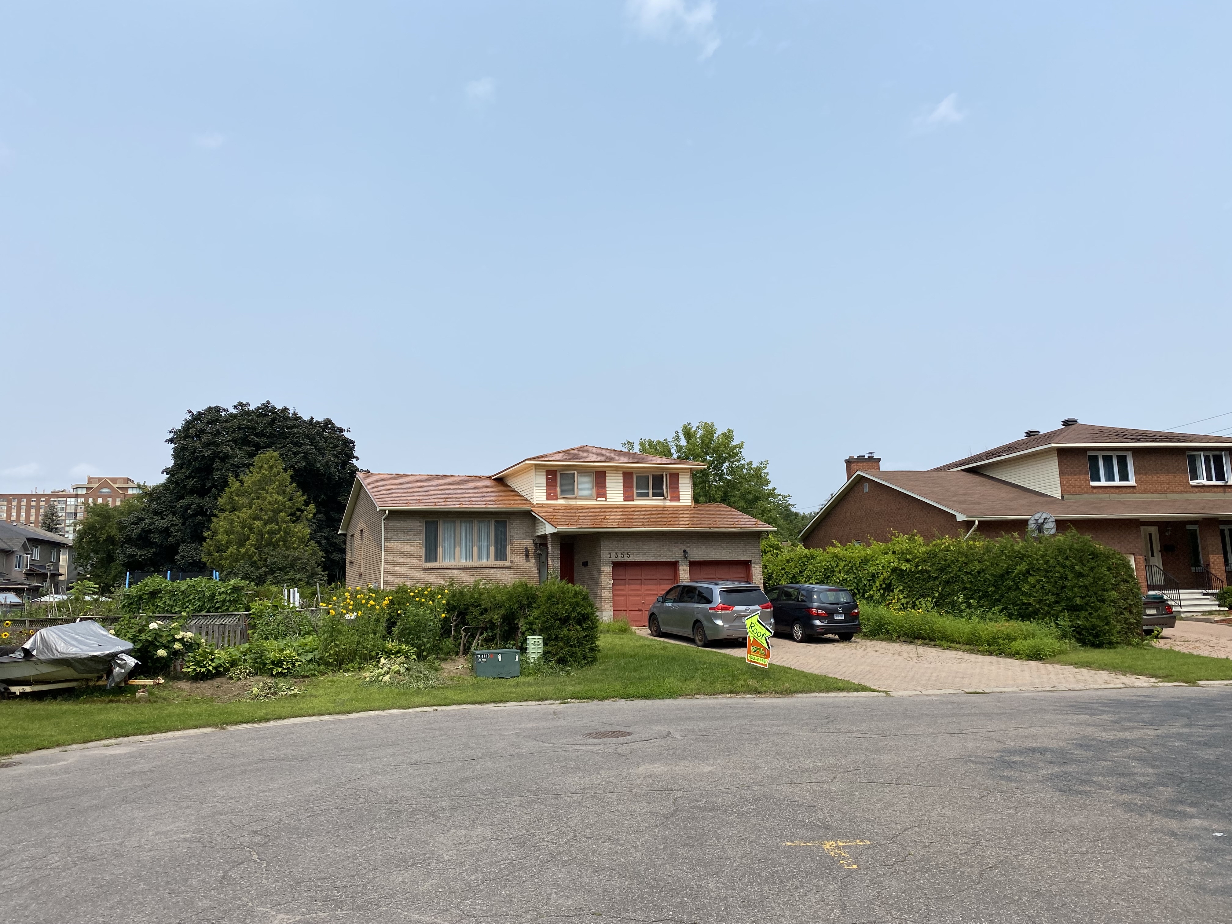 Street view of a two-storey brick home in Gloucester, ON with an Interlock Copper Penny aluminum slate metal roof and red garage doors.