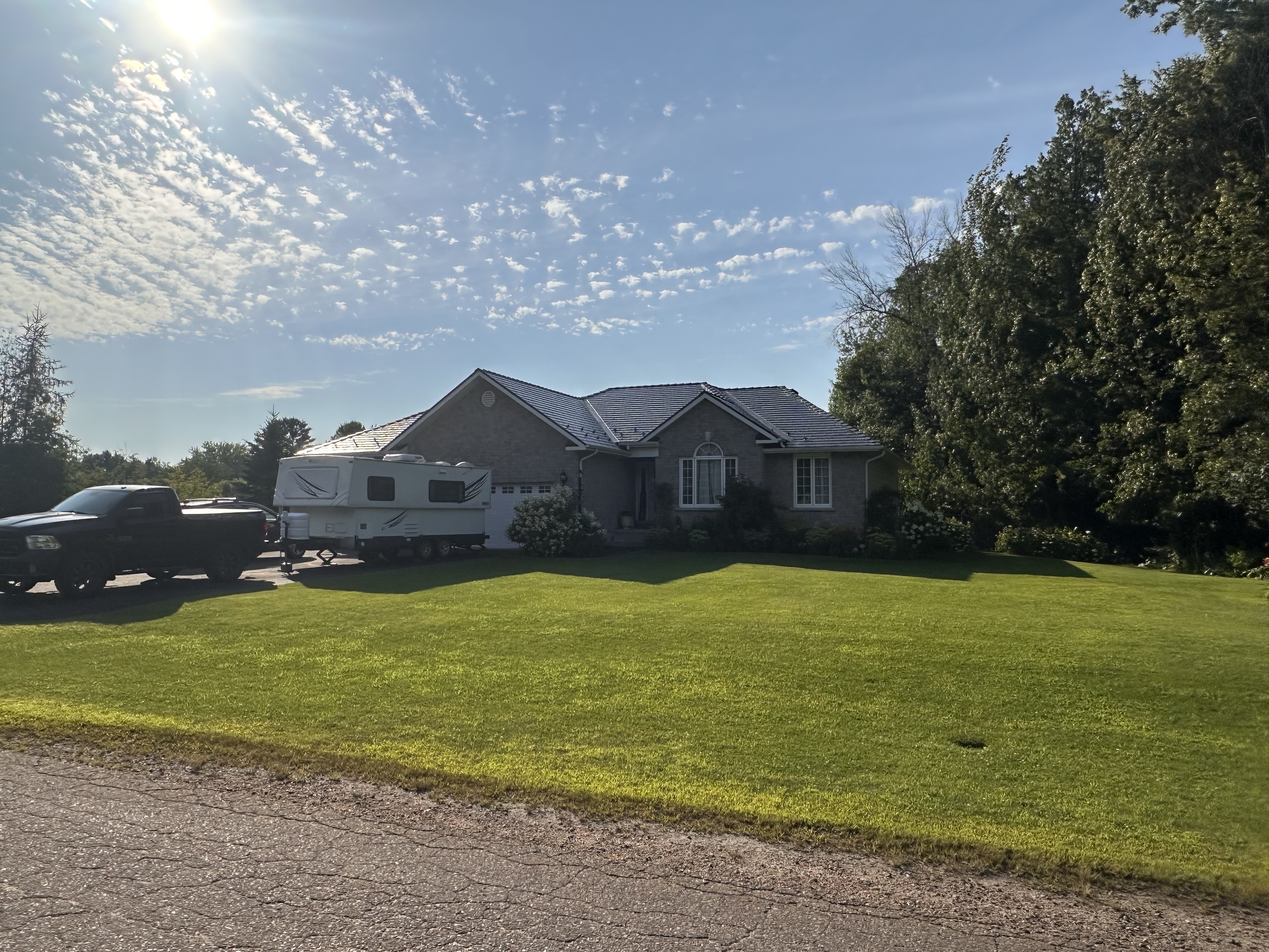 Single-storey ranch home in Pembroke ON with Interlock deep charcoal cedar shingle metal roof on a hip profile, surrounded by mature trees and lush lawn.