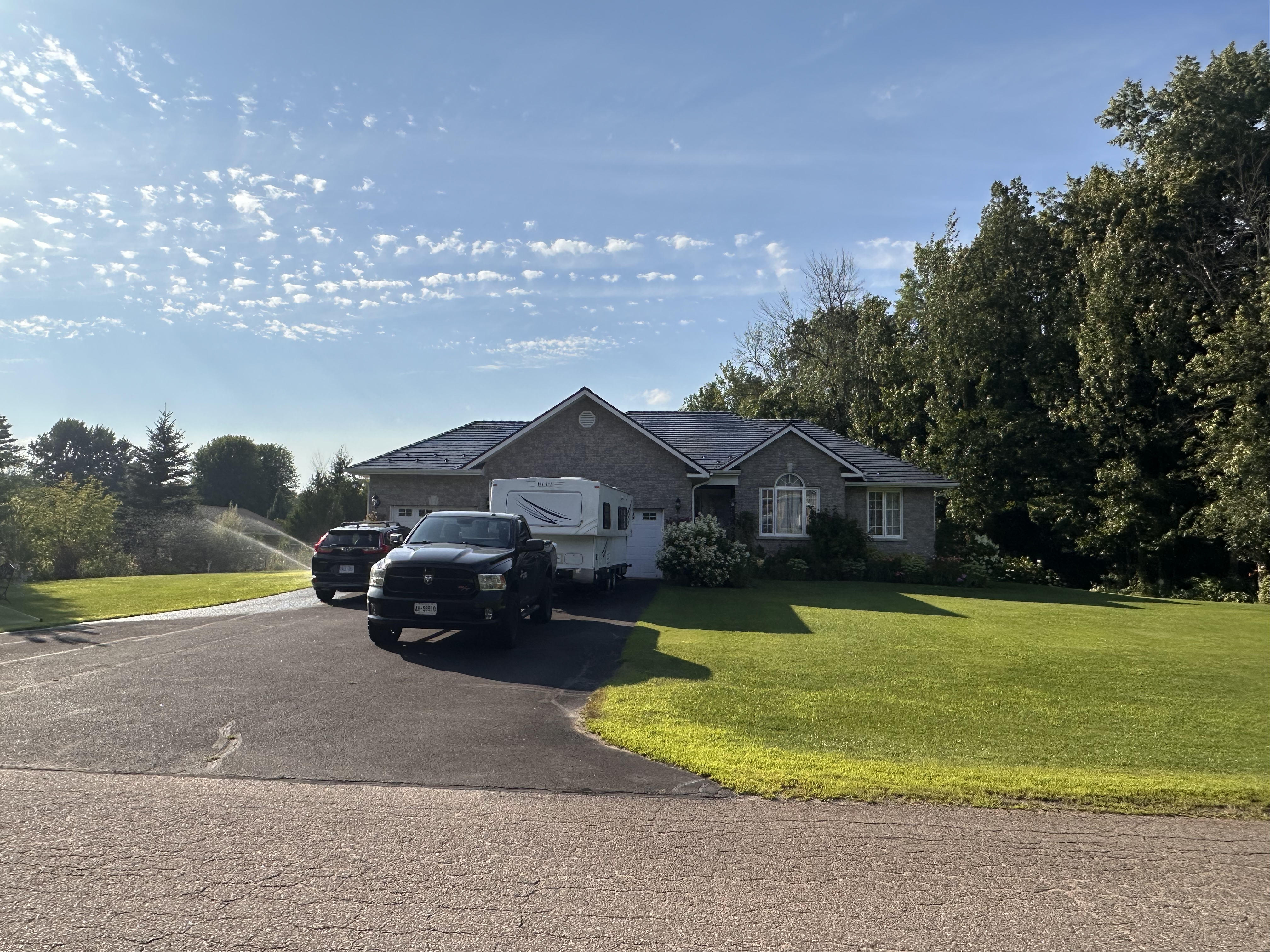 Ranch-style brick home with Interlock deep charcoal cedar shingle metal roof, multi-hip profile, viewed from front elevation on a sunny summer day.