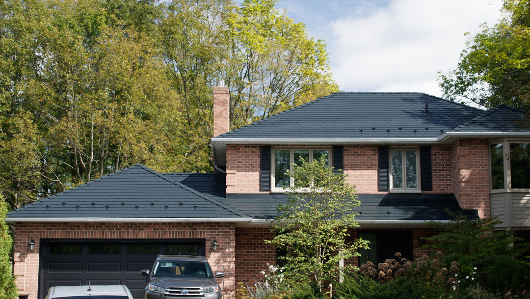 Two-storey brick Colonial home in Kingston, ON featuring a complex black Interlock aluminum slate metal roof with snow guards and brick chimney.
