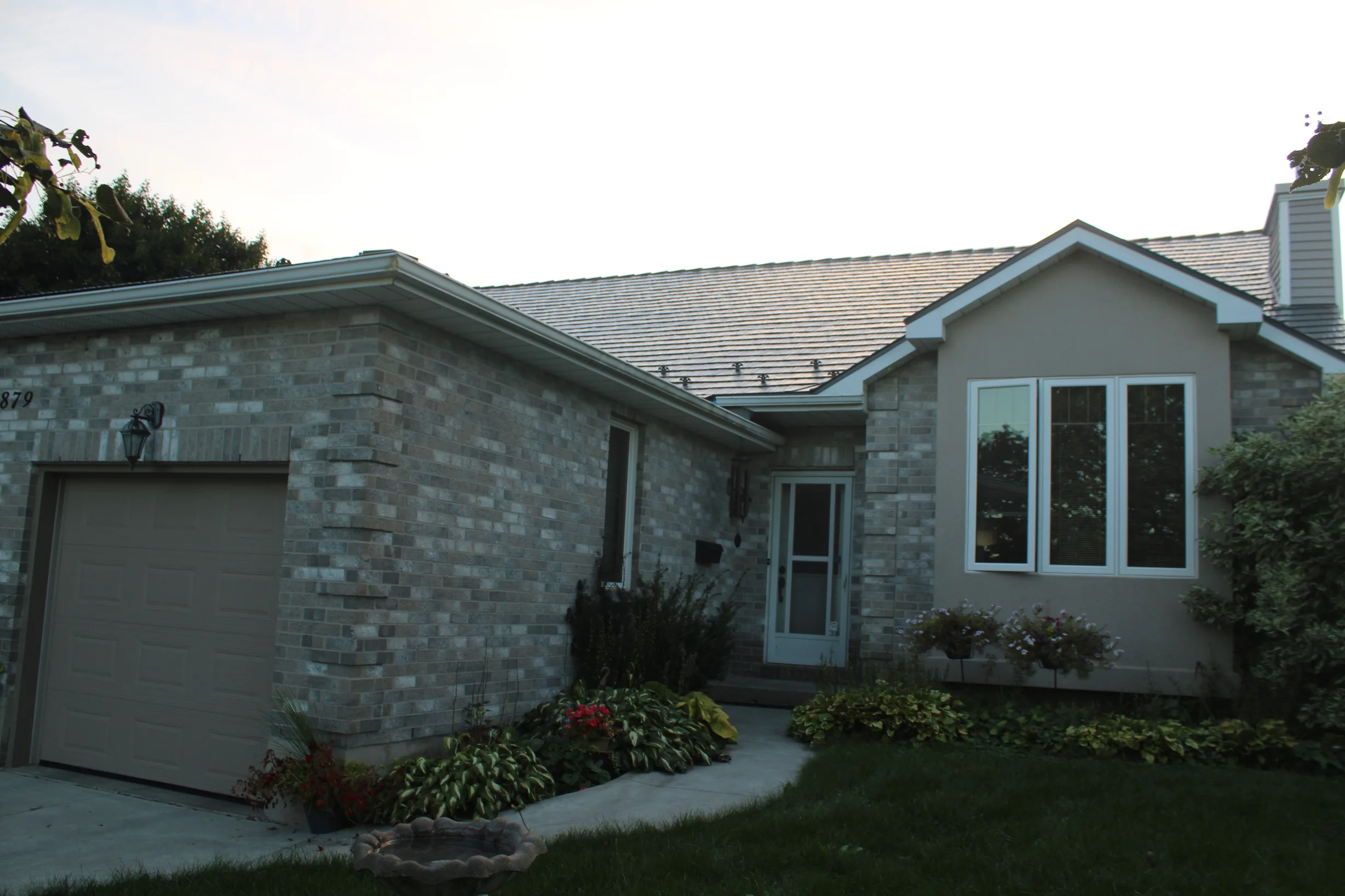 Deep Charcoal Interlock Cedar Shingle aluminum roof on a tan one-storey home with a metal roof among trees, Kingston, Ontario
