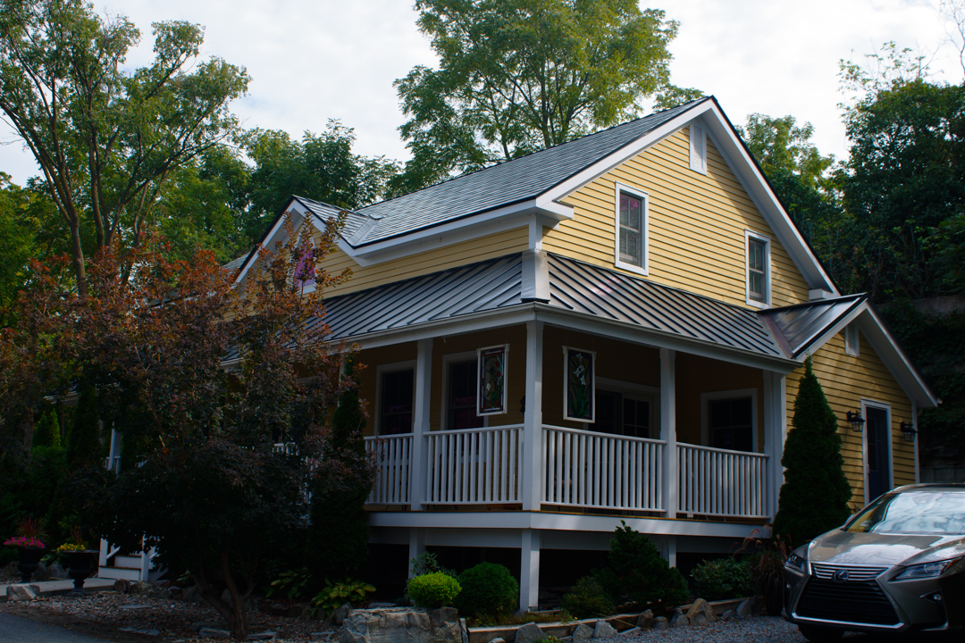 Yellow Craftsman home in Kingston ON with black Interlock aluminum slate metal roofing, wrap-around covered porch, and complex multi-plane roof.