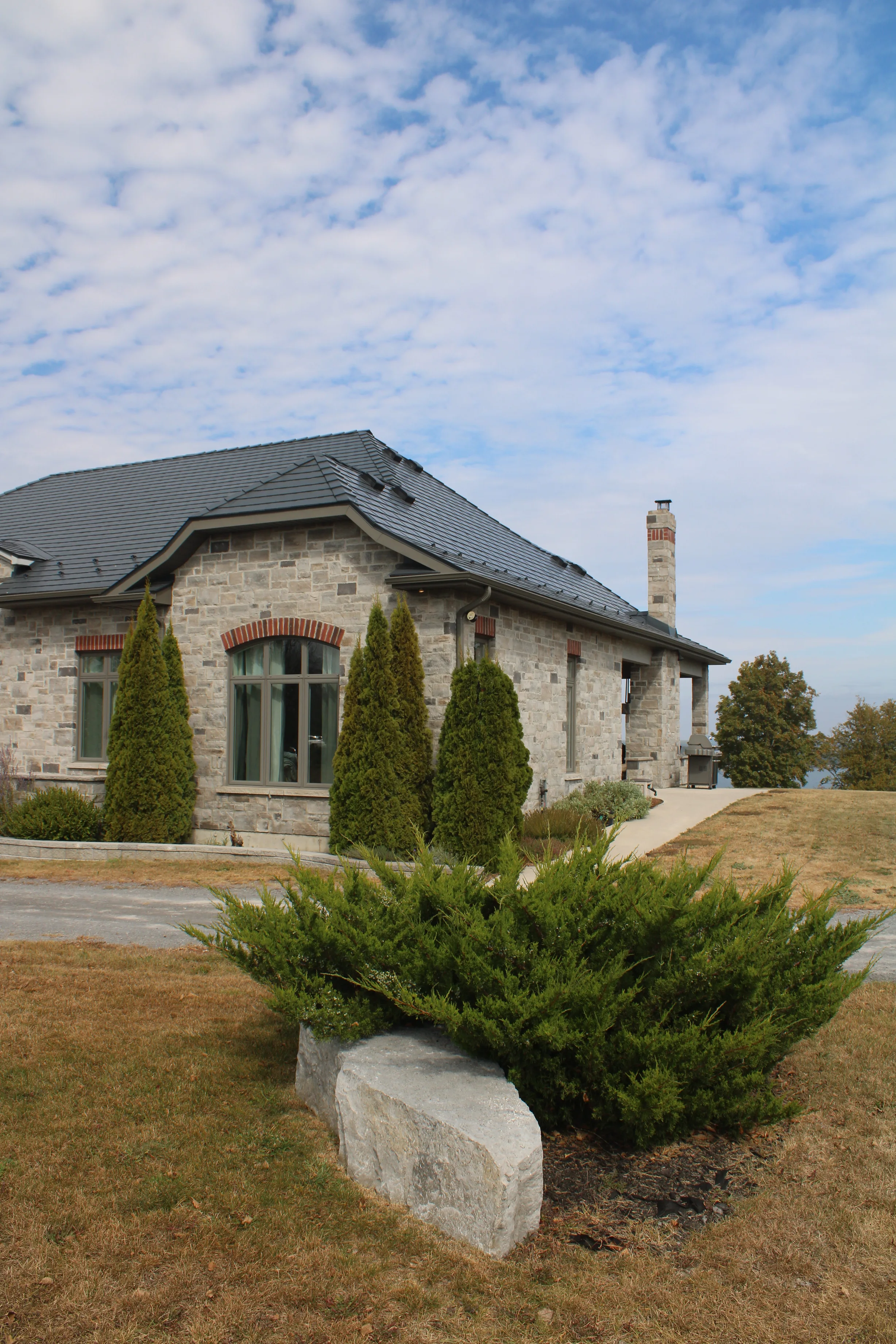 Deep Charcoal Interlock Slate aluminum roof on a Deep Charcoal metal roof on a stone Craftsman-style home, Picton, Ontario