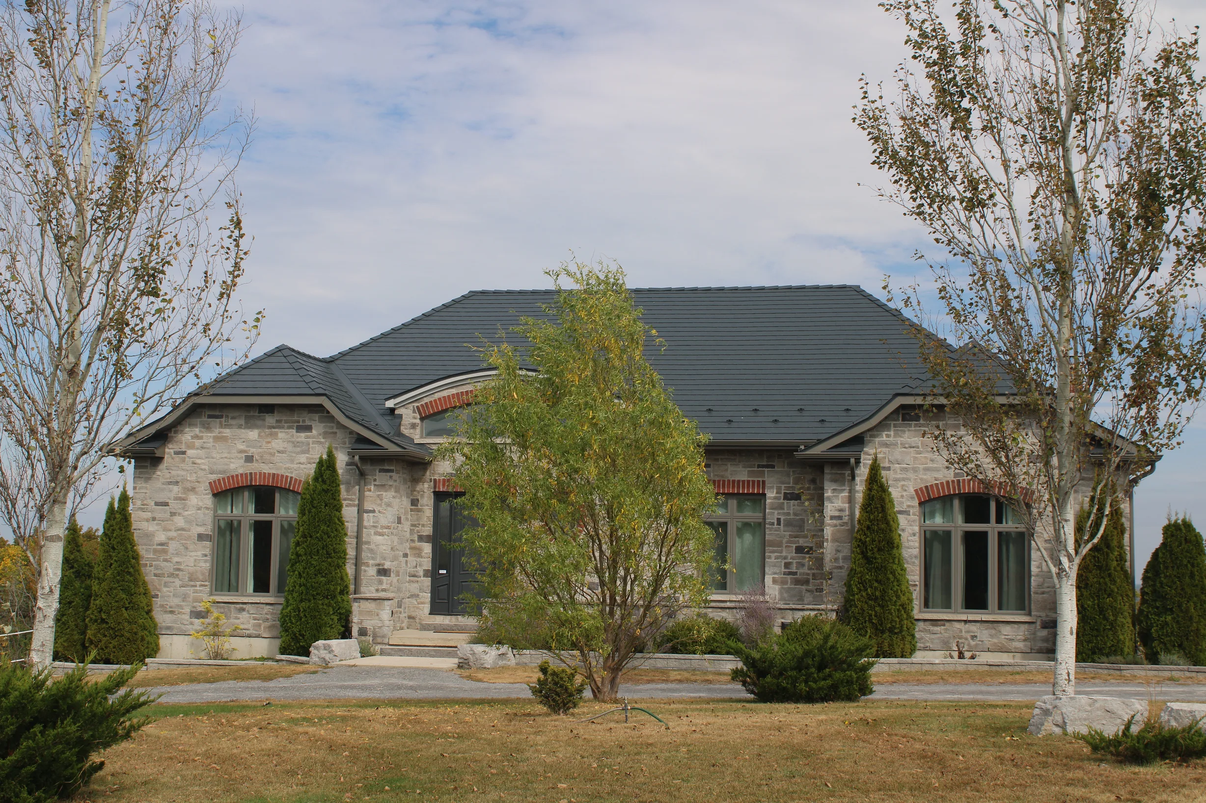 Deep Charcoal Interlock Slate aluminum roof on a stone ranch home with a metal roof in a rural setting, Picton, Ontario