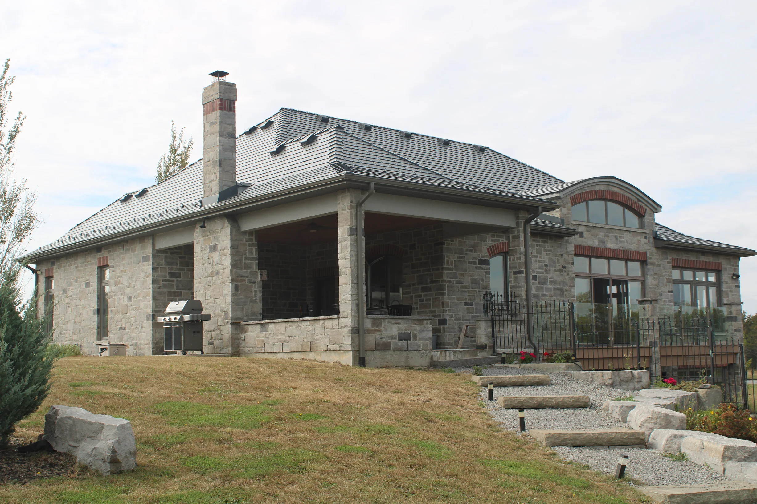 Deep Charcoal Interlock Slate aluminum roof on a stone house with a metal roof and chimney among trees, Picton, Ontario