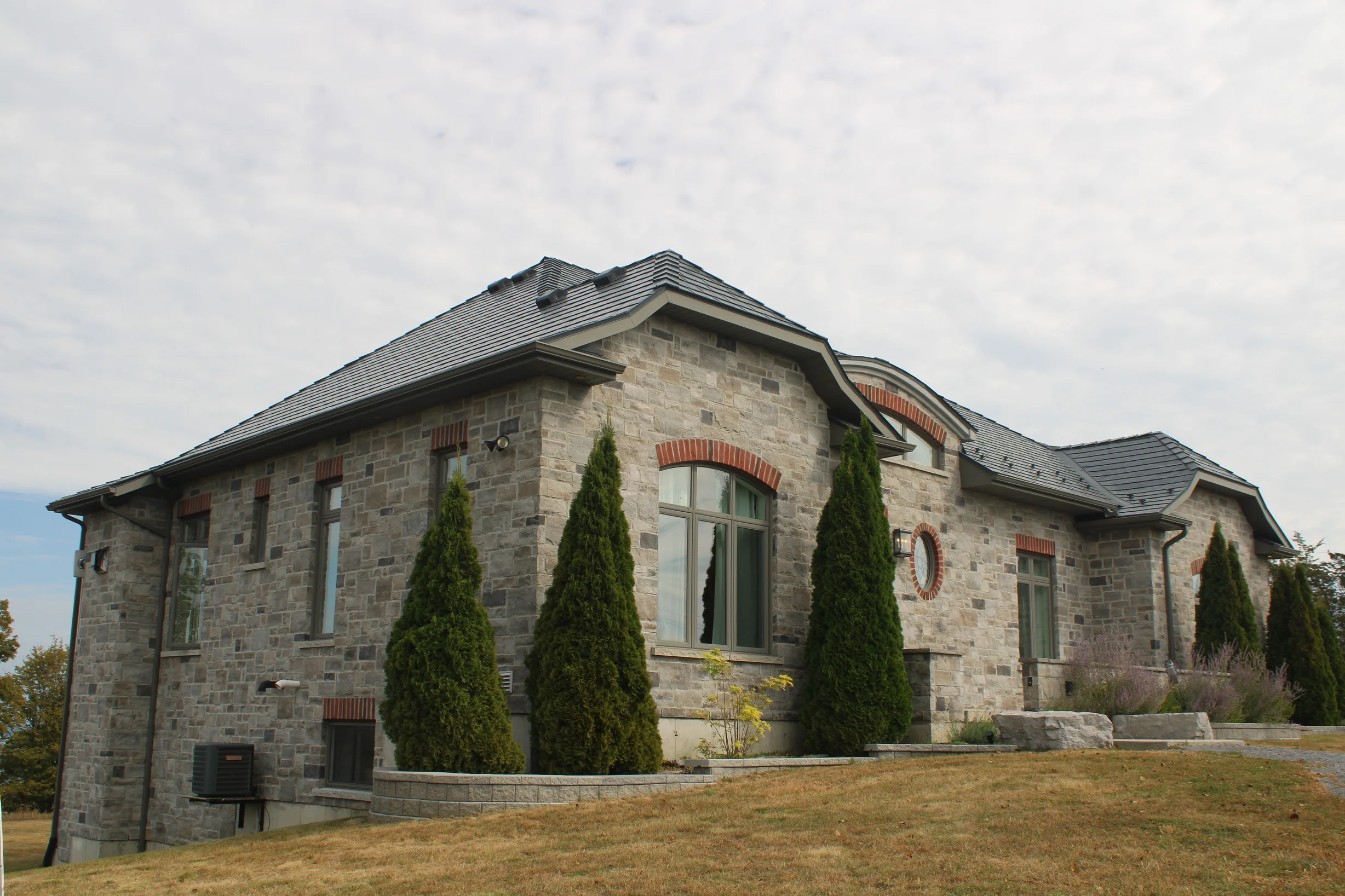 Deep Charcoal Interlock Slate aluminum roof on a grey stone house with a slate roof and a lawn, Picton, Ontario
