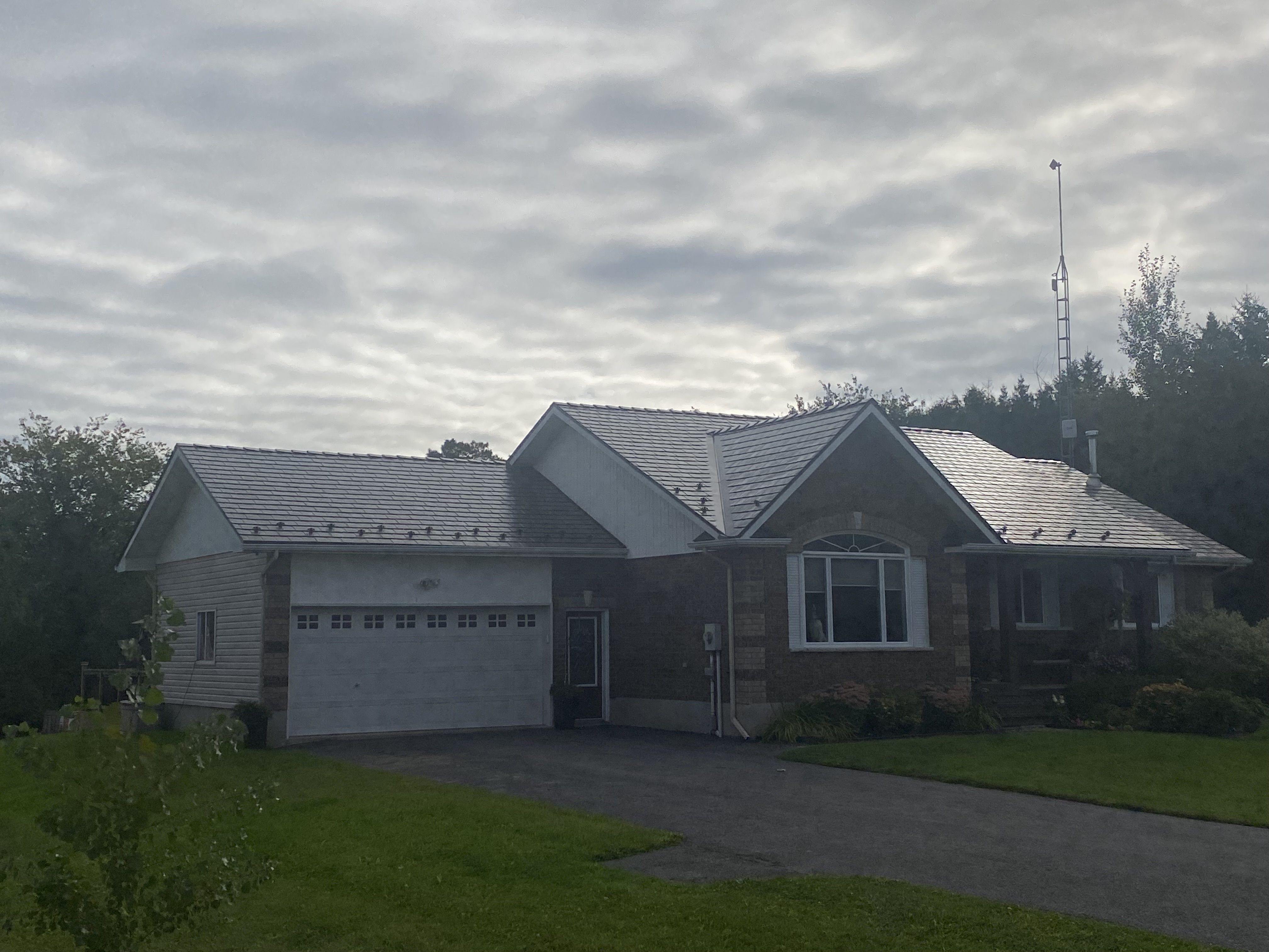 Ranch-style brick home in Winchester ON featuring Interlock Tudor Brown aluminum slate metal roofing with multi-gable complex roof profile under overcast skies.
