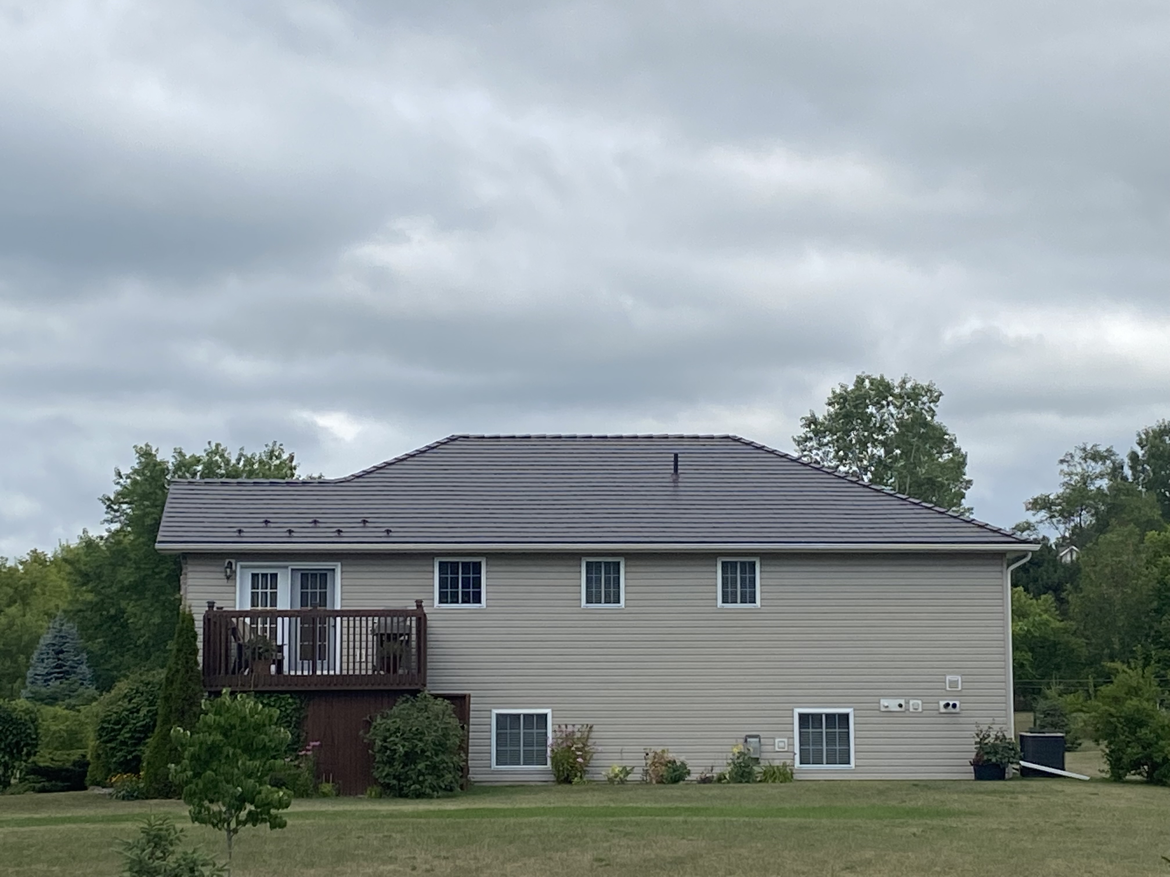Rear elevation of a two-storey rural home in Frankford, ON featuring an Interlock Tudor Brown cedar-shingle aluminum hip roof with snow guards and a raised wood deck.
