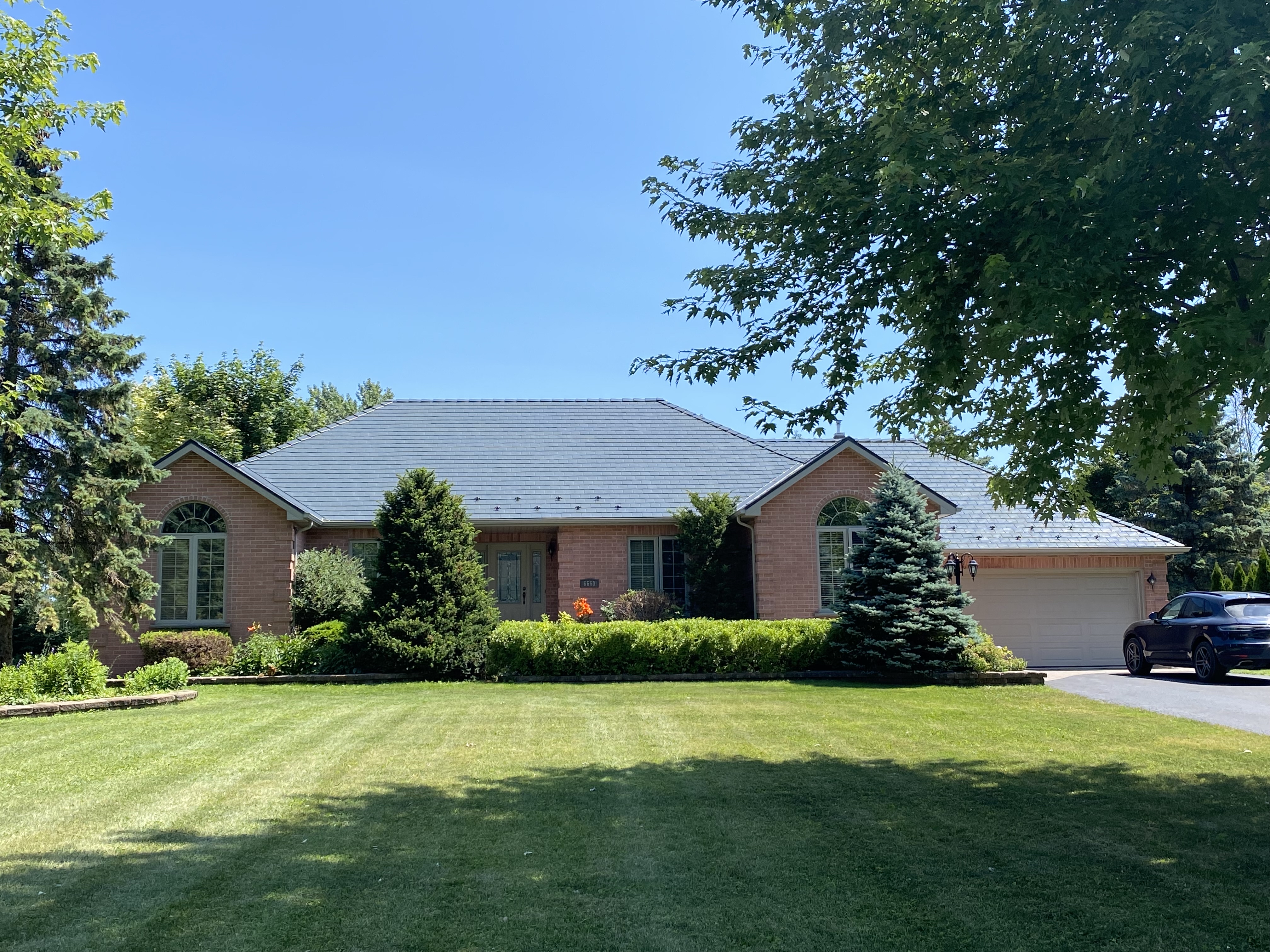Single-storey brick ranch home in Cornwall, ON with a deep charcoal Interlock aluminum slate hip roof, two-car garage, and manicured lawn.