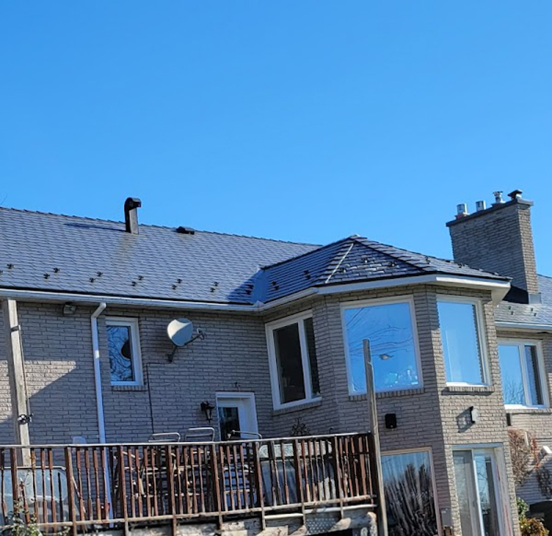Rear elevation of a two-storey brick Colonial home in Nepean, ON featuring Interlock deep charcoal aluminum slate roofing with complex hip geometry and twin chimneys.