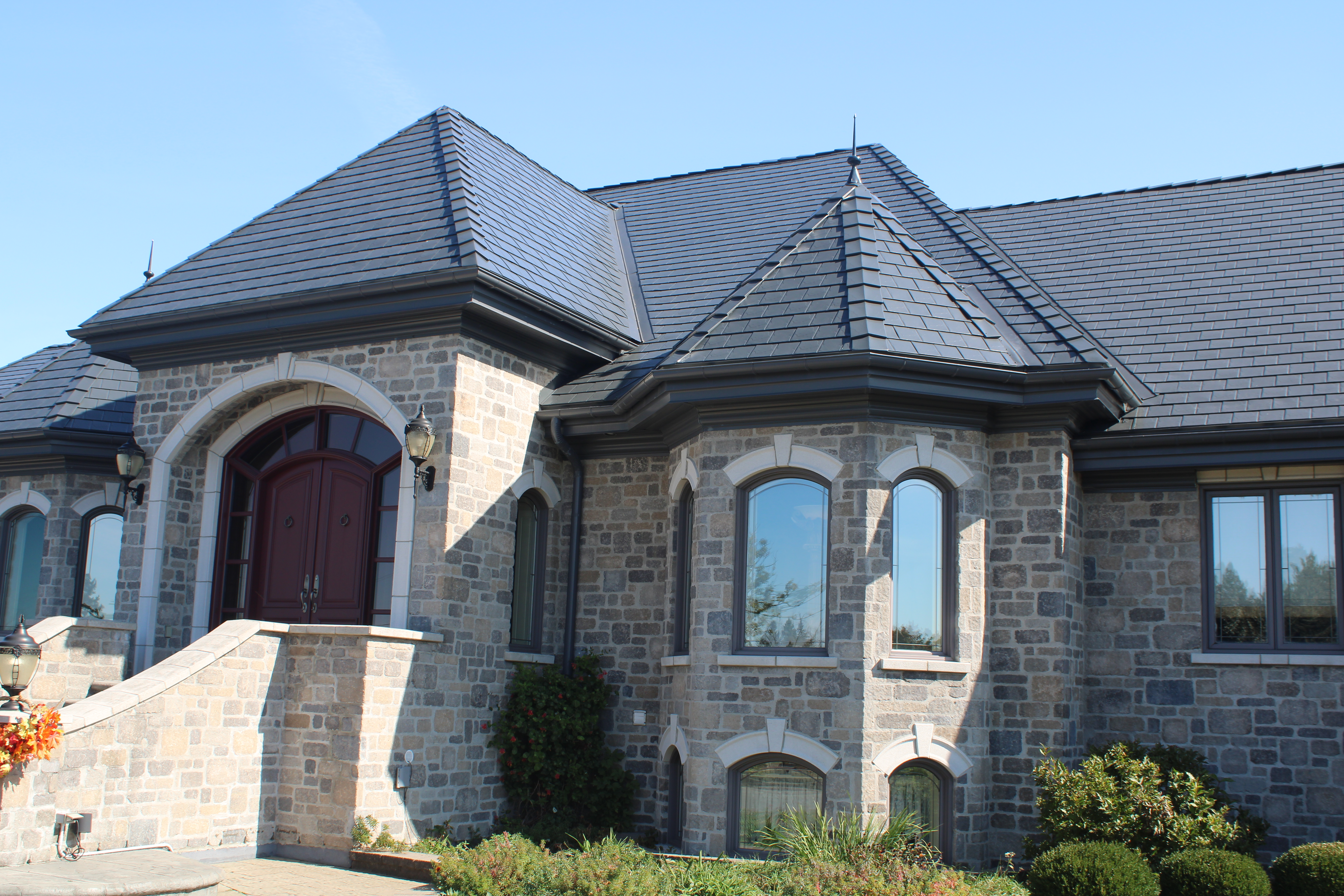 Luxury stone manor in Alexandria ON featuring Interlock deep charcoal aluminum slate roofing with multi-hip complexity, prominent turret, and arched entry.