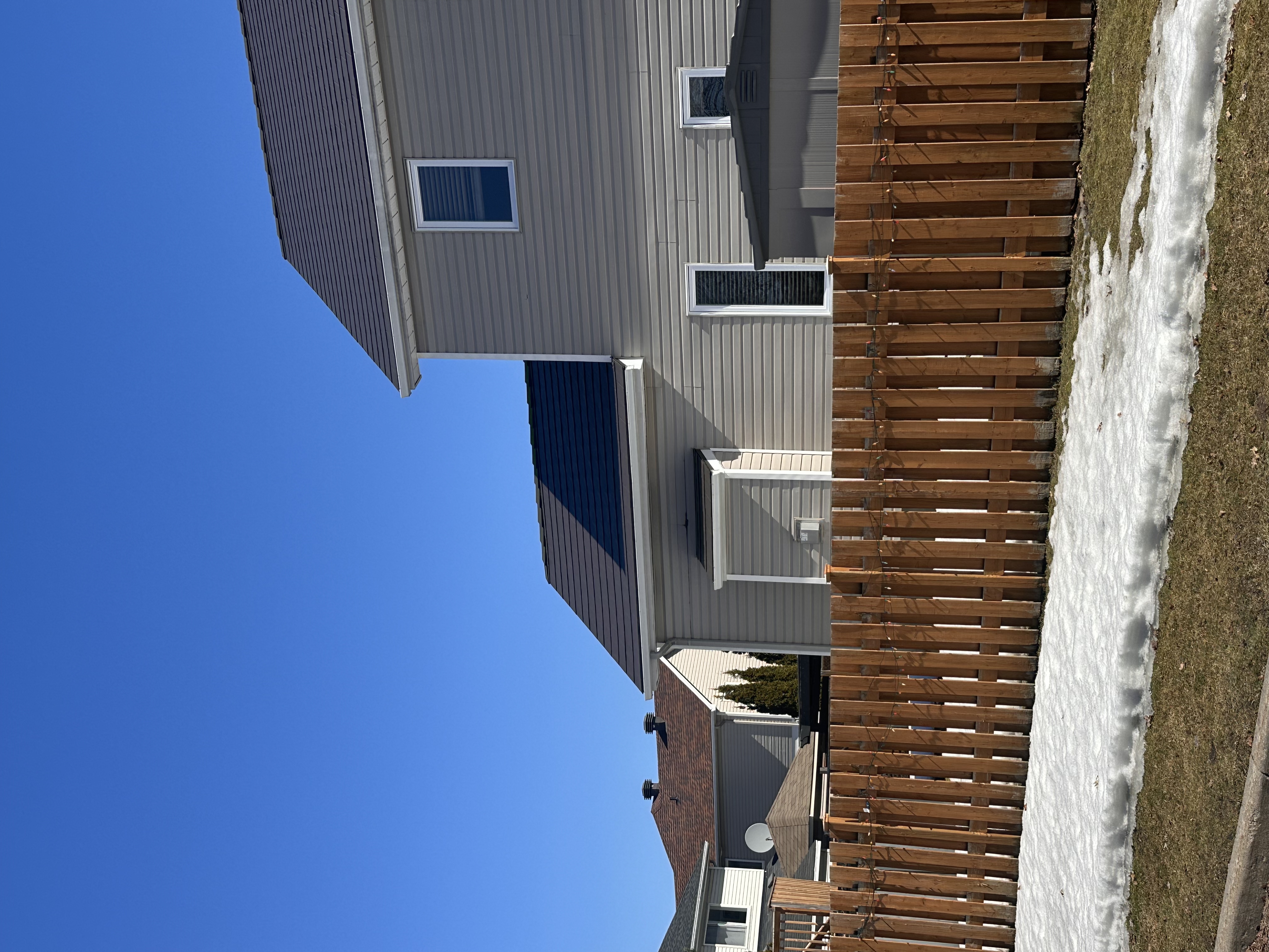 Tudor Brown Interlock aluminum slate metal roof on a two-storey suburban home in Ottawa, viewed from rear-left with a wooden fence in the foreground.