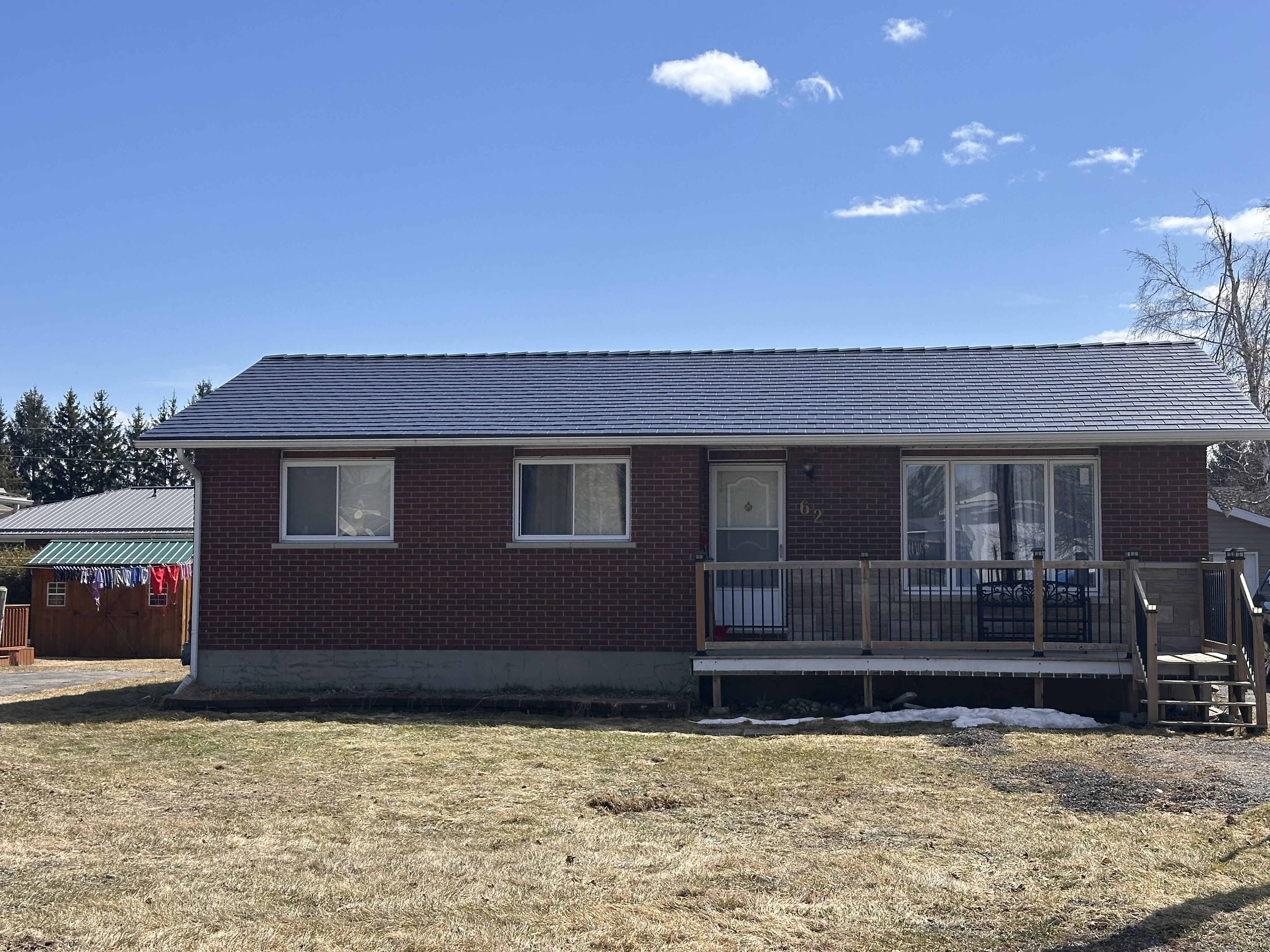 Front elevation of a brick ranch home in Chesterville, ON featuring a black Interlock aluminum slate metal roof with a low-pitch simple gable and front deck.