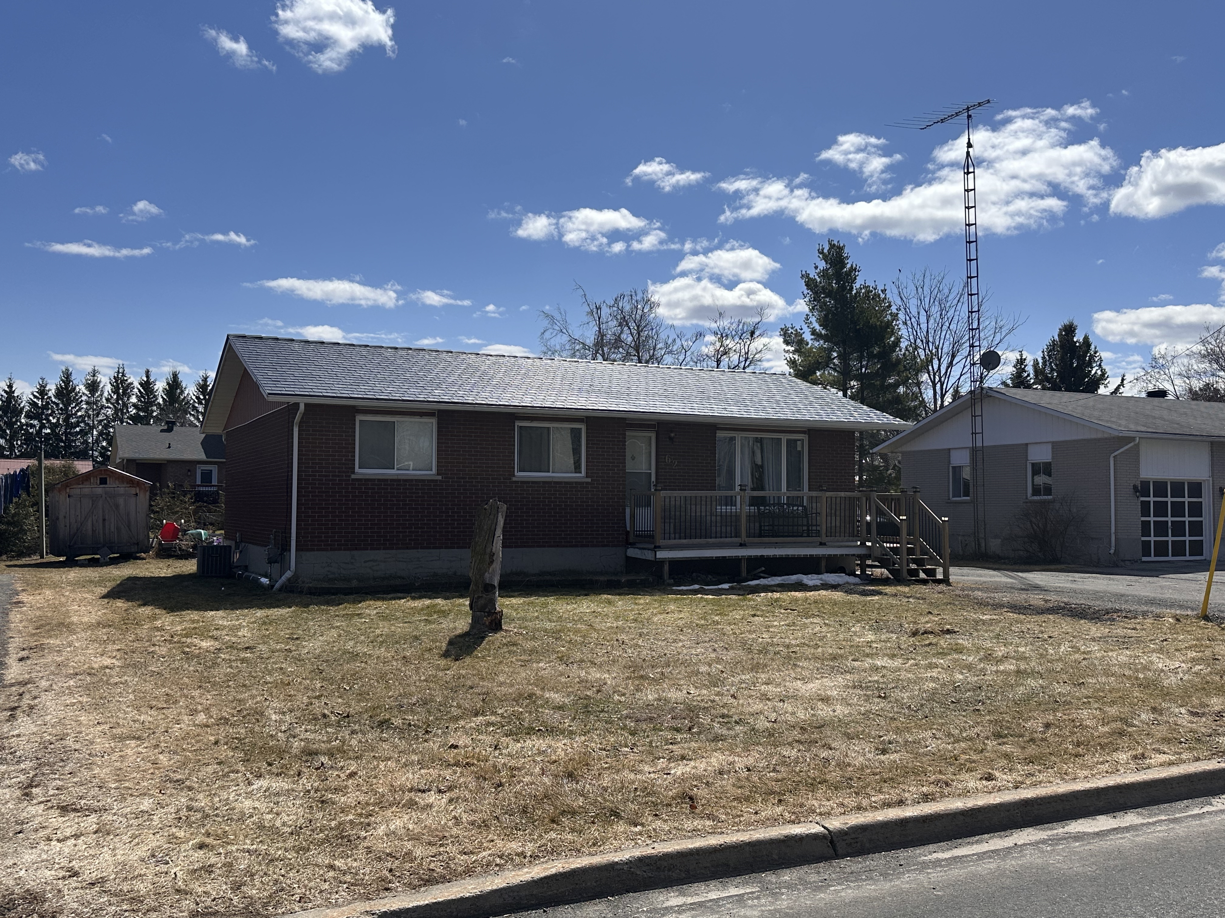 Front elevation of a 1-storey brick ranch home in Chesterville, ON, featuring a low-pitch Interlock black aluminum slate metal roof with light snow dusting.