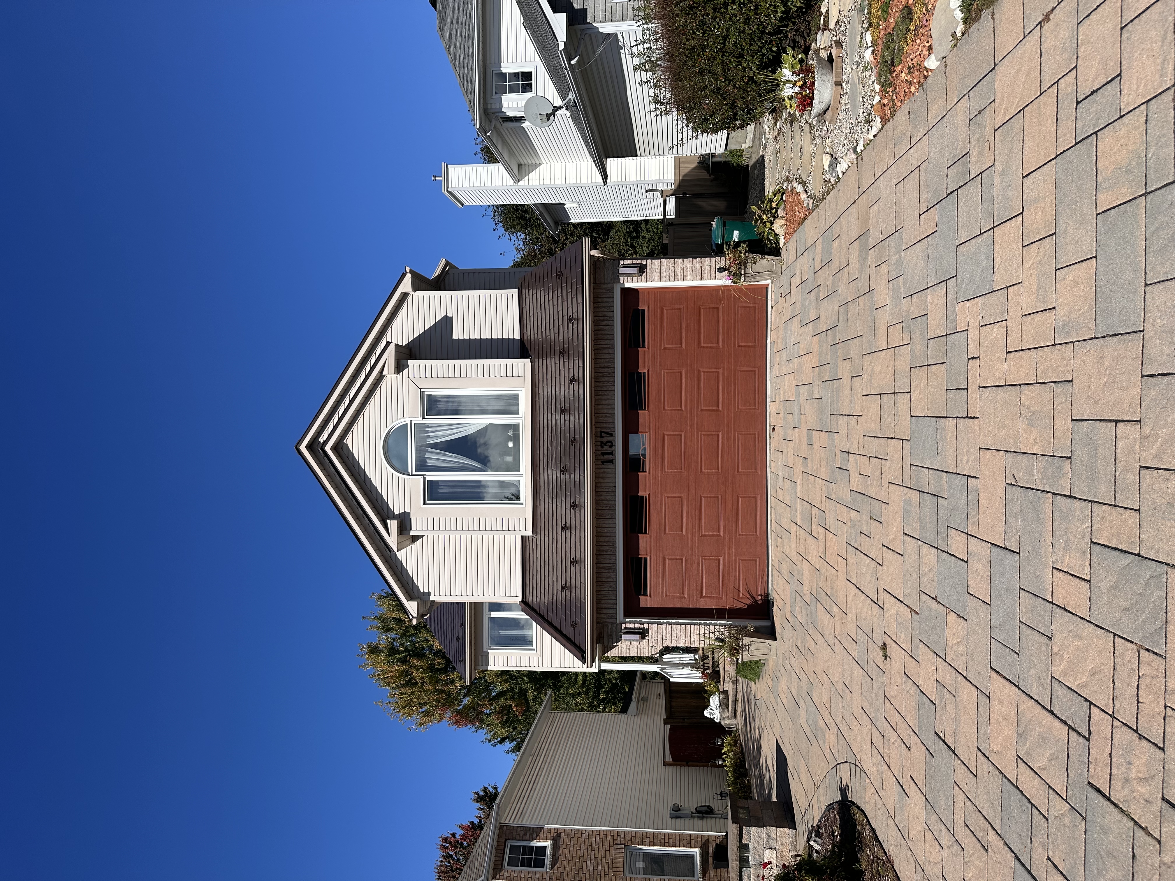 Two-storey suburban home with Interlock Colonial Brown aluminum slate roof, brown gable profile, arched dormer window, and interlocking paver driveway.