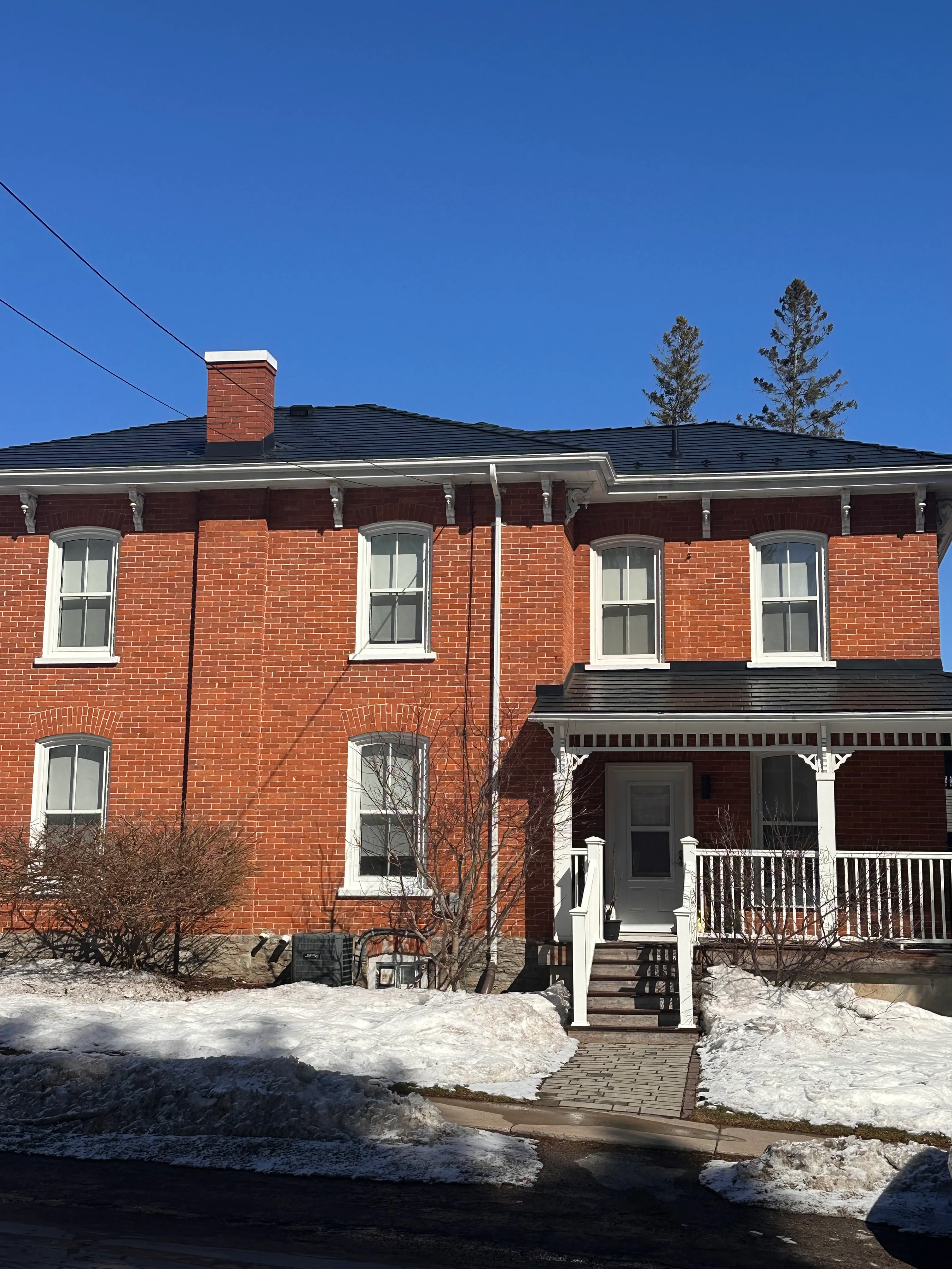 Black Interlock Slate aluminum roof on a red brick two-storey home with dormers in a rural winter, Prince Edward, Ontario