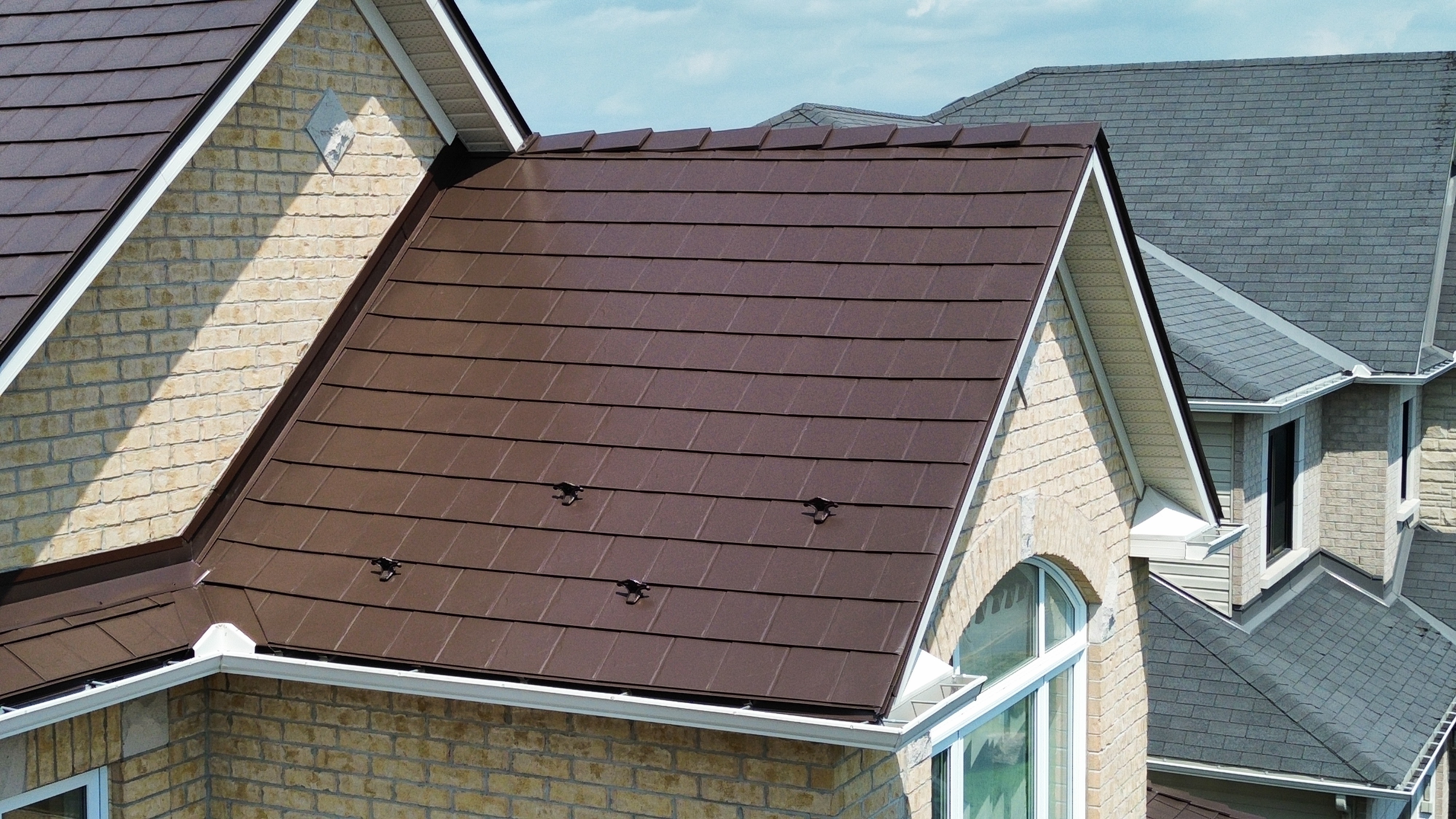 Colonial Brown Interlock aluminum slate metal roof on a 2-storey suburban home with snow guards, brick exterior, and complex multi-gable roofline.