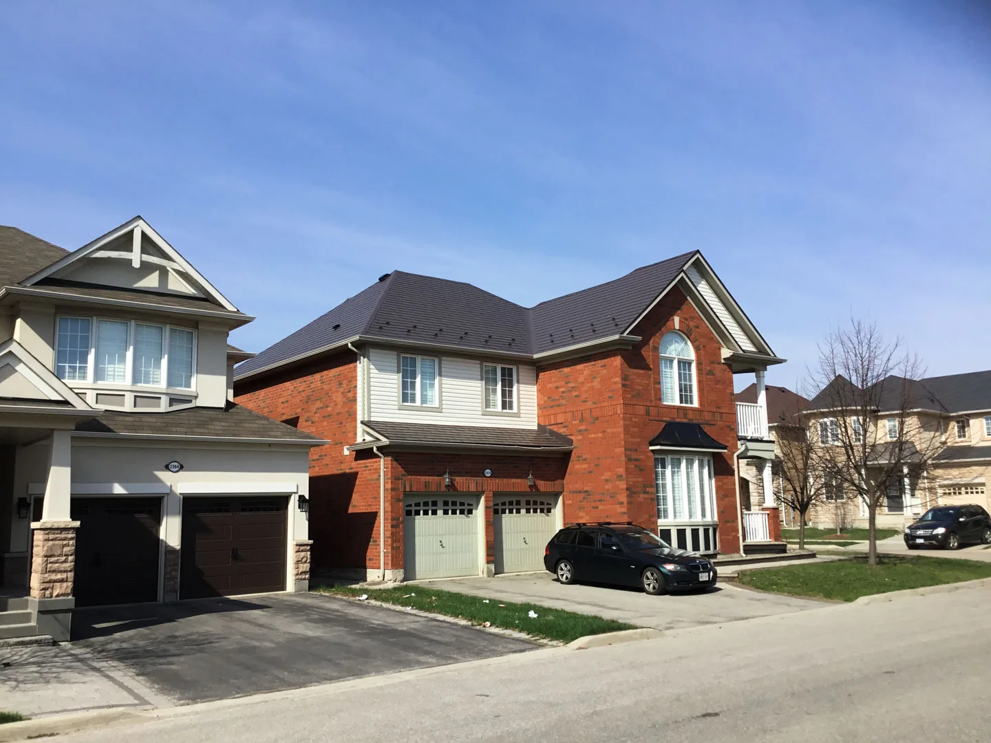 Two-storey red-brick suburban home with Tudor Brown Interlock aluminum shingle metal roofing featuring a multi-hip complex roof profile, Richmond Hill, ON.