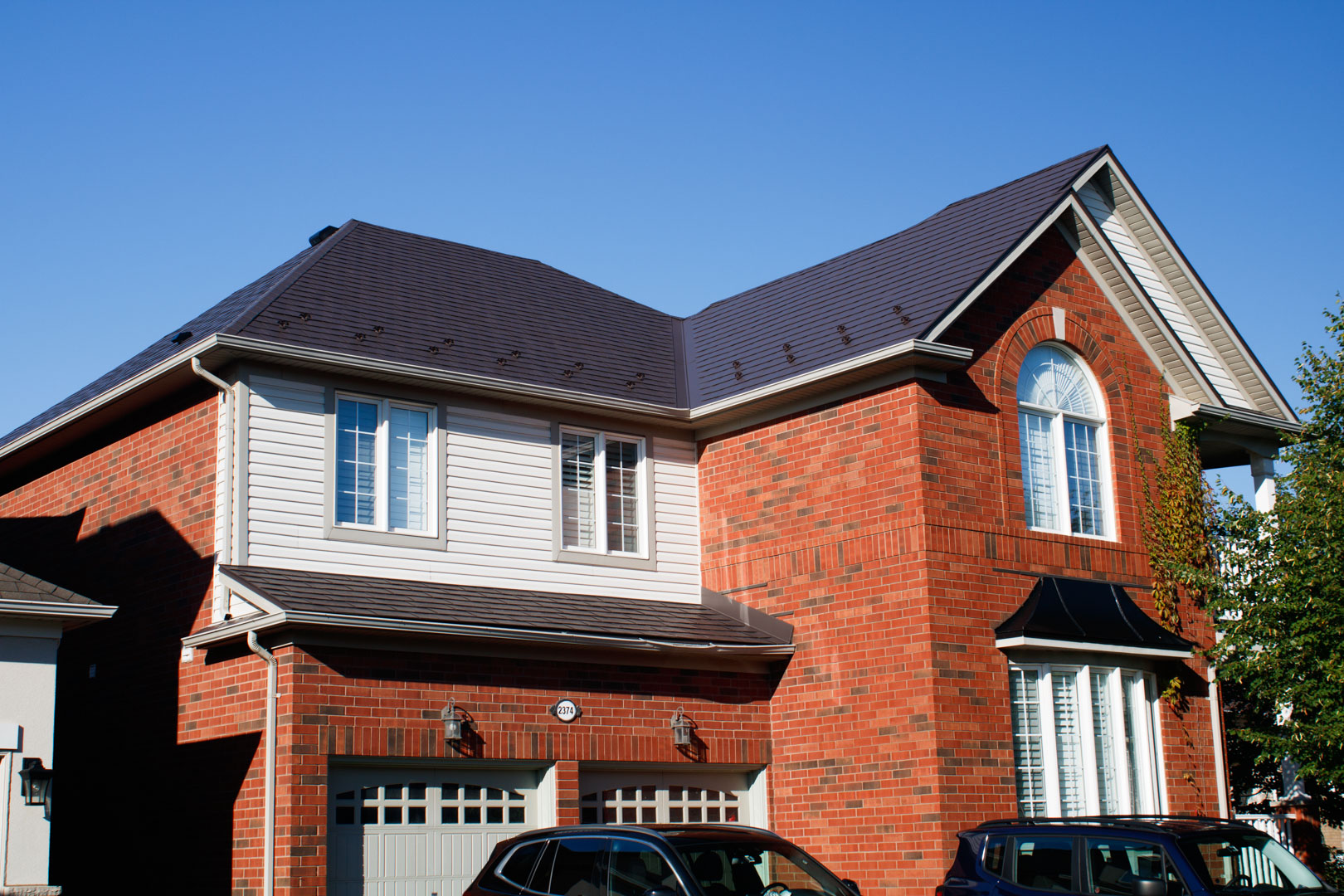 Two-storey brick home in Richmond Hill with complex multi-hip Interlock Tudor Brown aluminum shingle roof, arched window, and double garage.