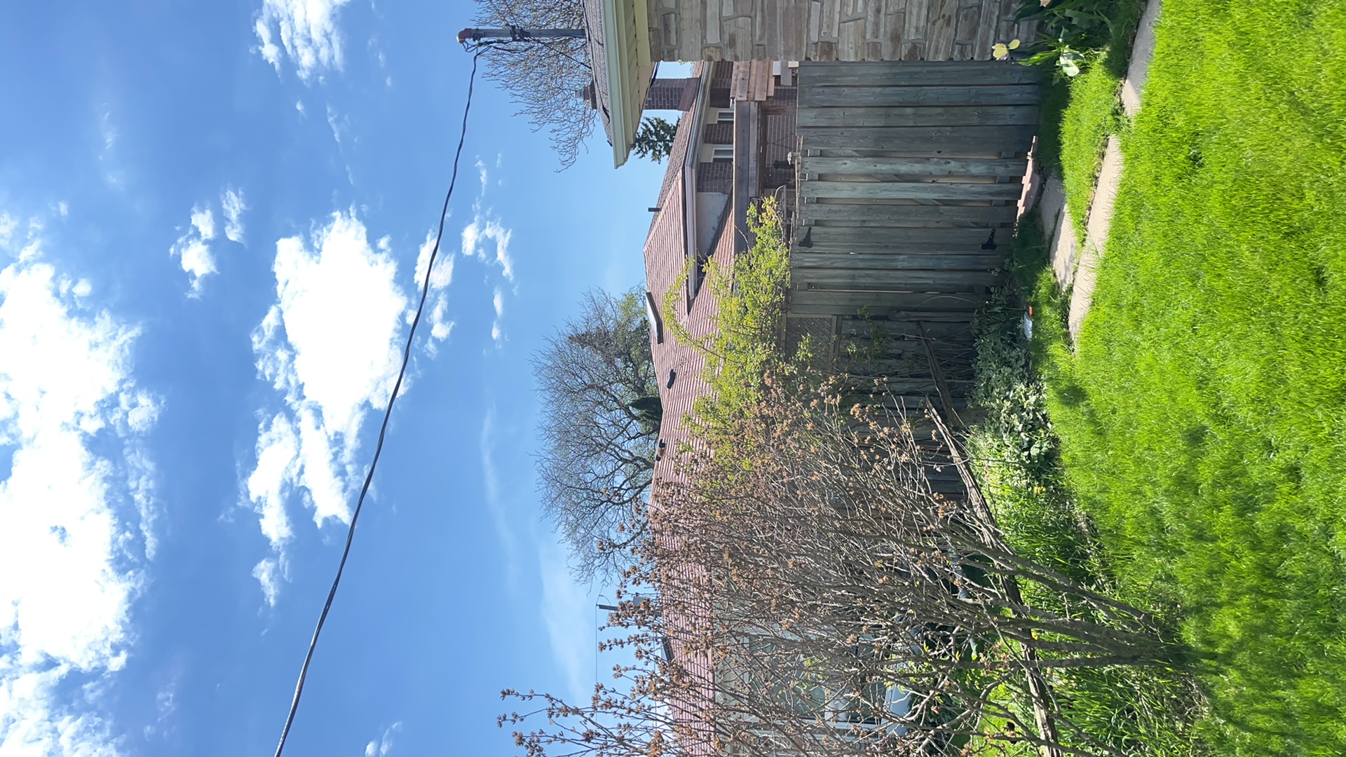 Rear yard view of a suburban single-family home with a hip roof in aged copper Interlock aluminum shingles, partially obscured by fence and shrubs.