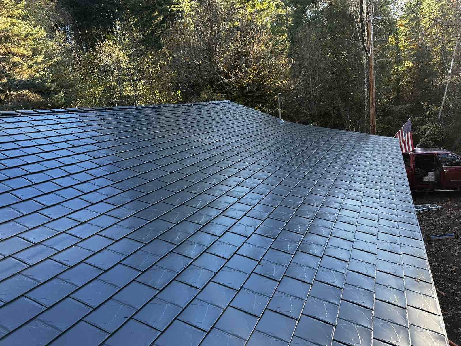 Overhead view of a black Interlock aluminum slate metal roof on a single-family home surrounded by fall foliage in Alsea, OR.