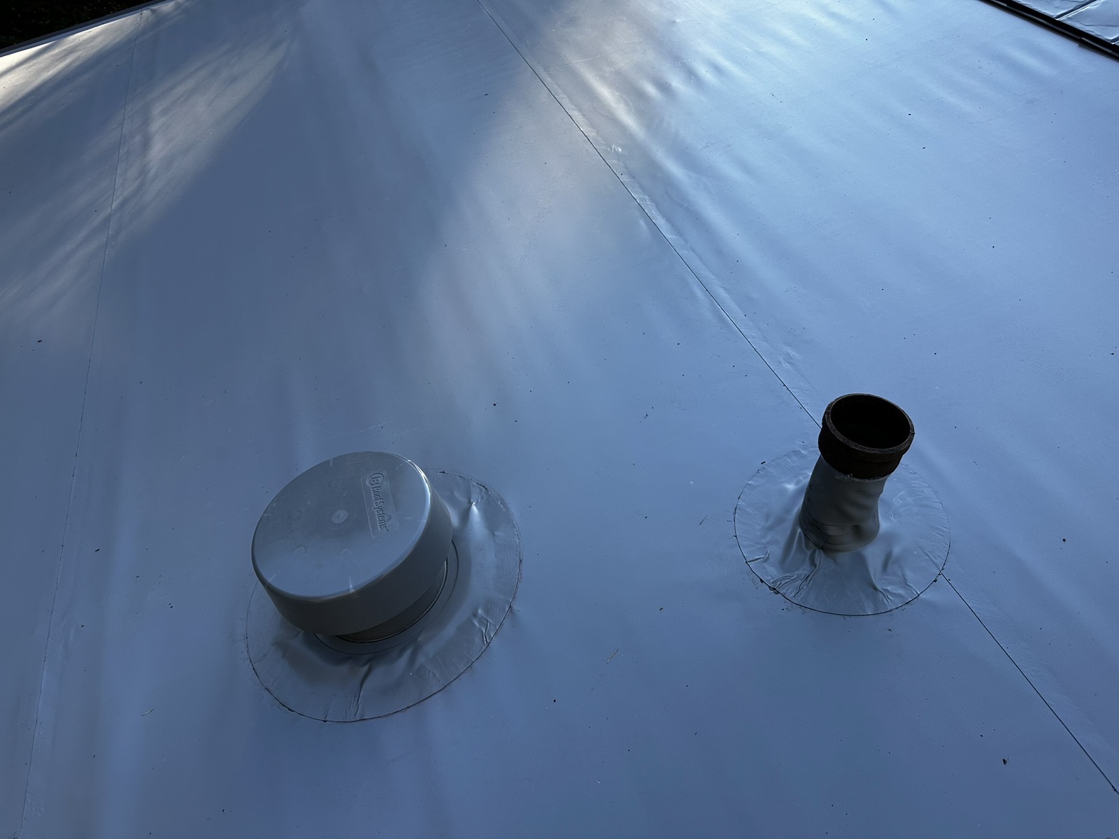 Close-up of a white TPO or membrane flat roof showing two penetrations: a capped roof vent and an open vent pipe with flashing boots.